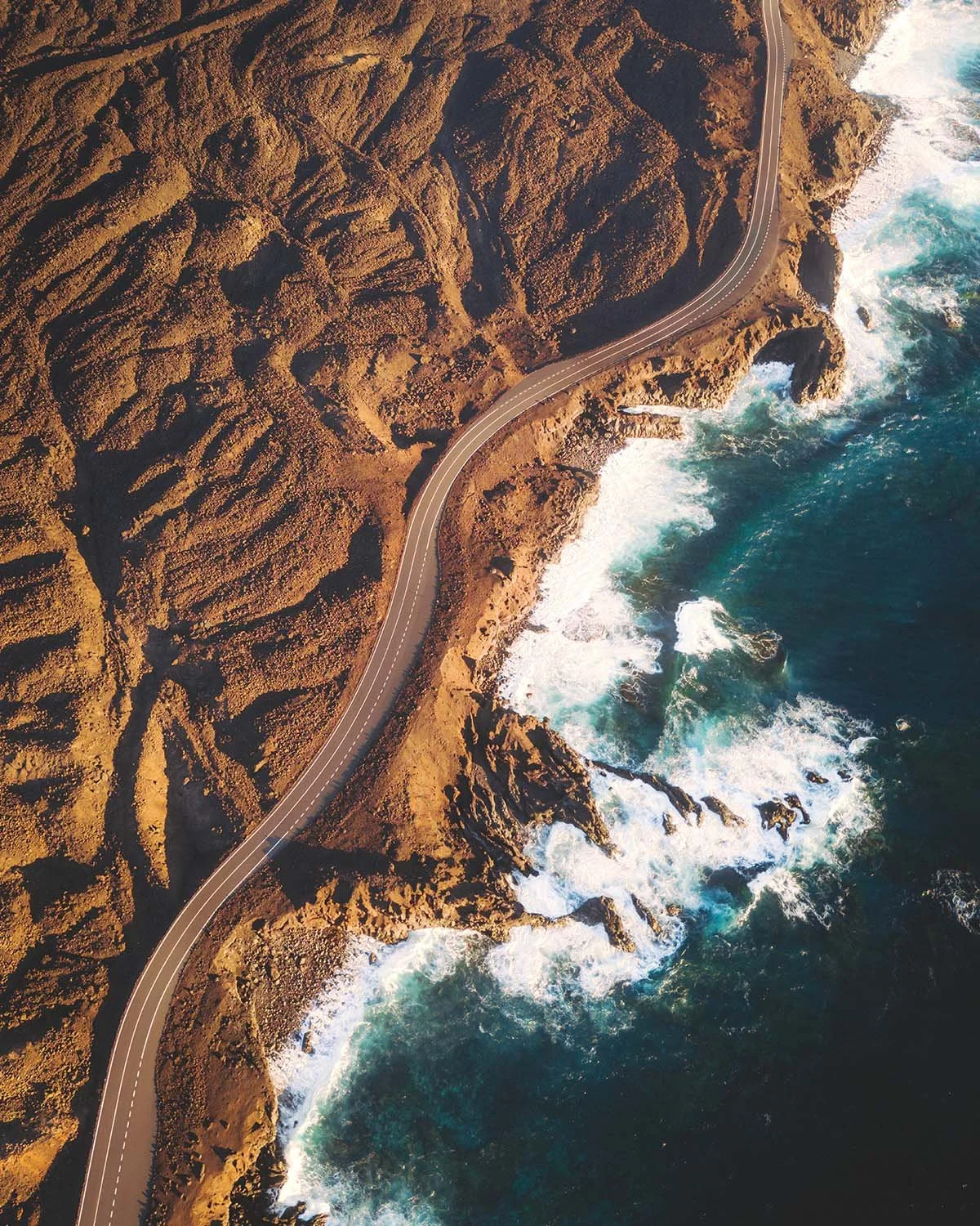 Vue aérienne spectaculaire de la route longeant la côte volcanique de Lanzarote, où les champs de lave noire rencontrent l'écume blanche de l'océan.