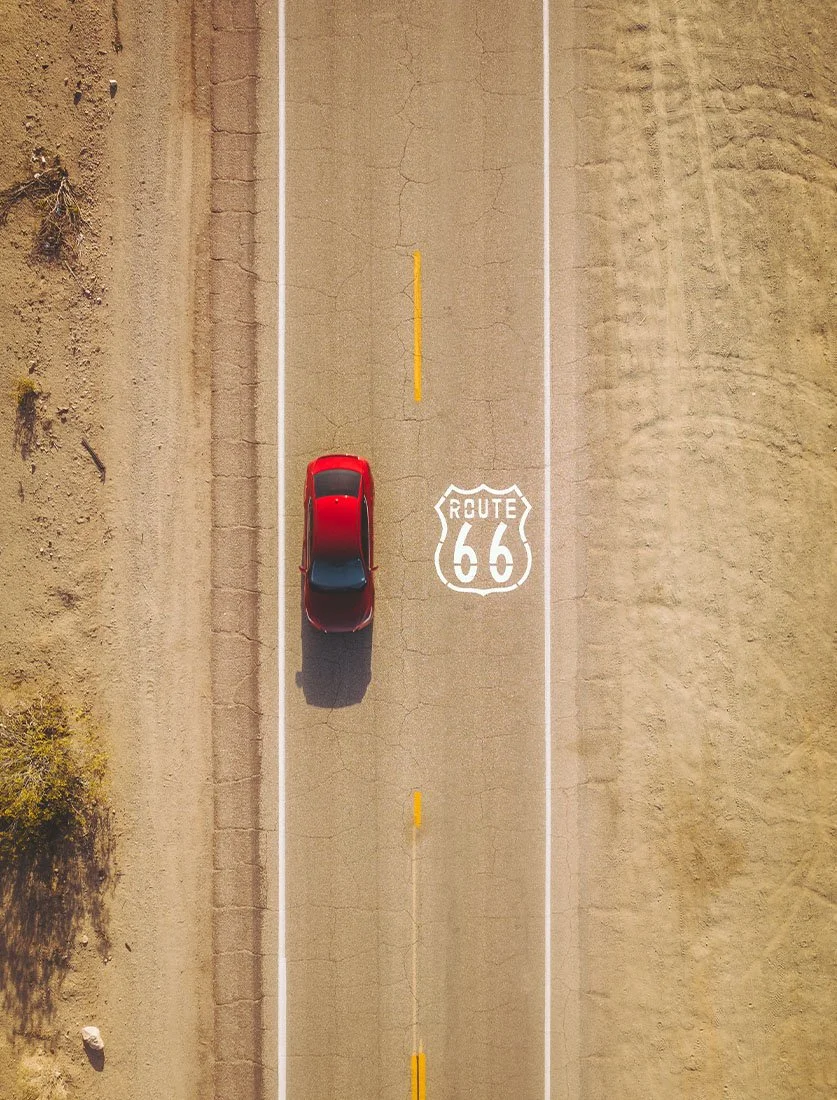Vue aérienne iconique et minimaliste d'une voiture rouge sur la Route 66 aux États-Unis. Photographie de voyage et roadtrip américain.