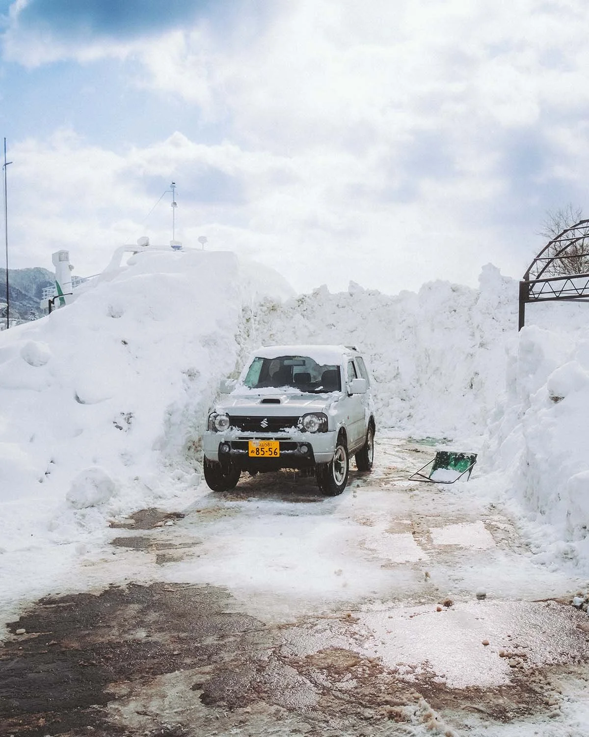 Un Suzuki Jimny (Kei car) stationné dans une alcôve creusée dans un mur de neige massif. Le véhicule ultime pour l'aventure hivernale au Japon photographié par Dimitri Weber.