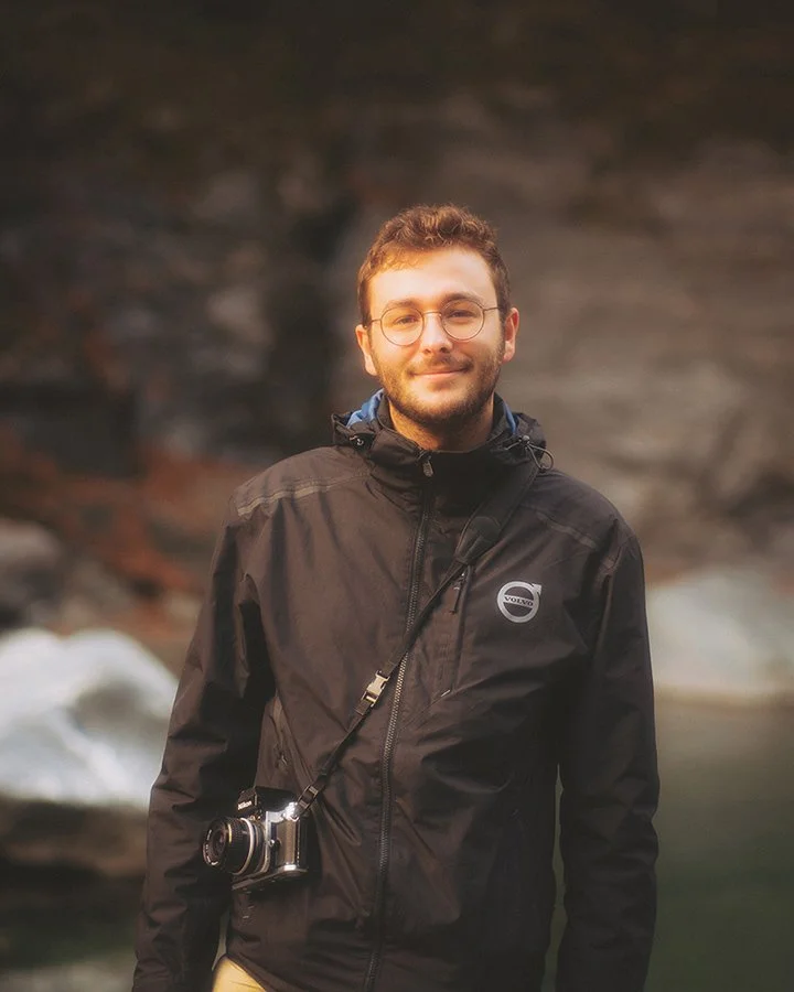 Portrait souriant de Dimitri Weber, photographe et vidéaste professionnel basé en Île-de-France, portant un appareil photo en bandoulière. Image de présentation du fondateur.