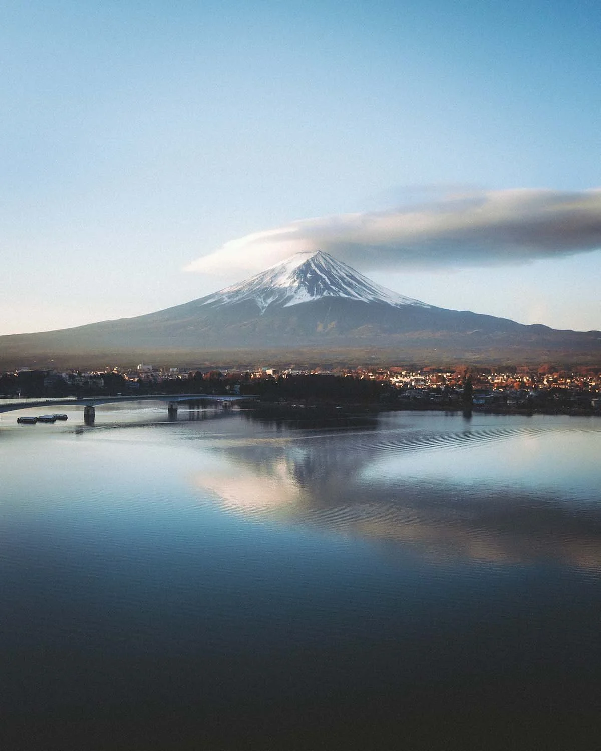 Le Mont Fuji coiffé d'un immense nuage lenticulaire (Kasagumo) se reflétant dans les eaux calmes du lac Kawaguchiko. Paysage iconique japonais capturé au lever du soleil.