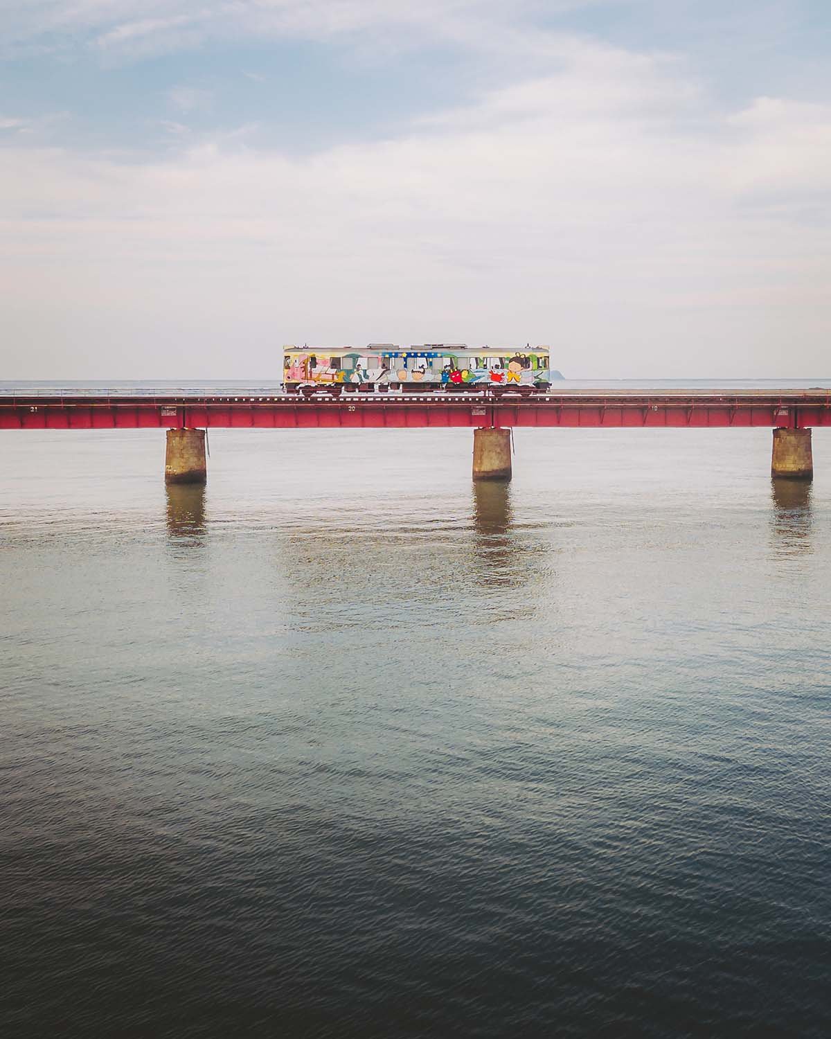 Le train pittoresque de la Kyoto Tango Railway traversant le célèbre pont rouge au-dessus de la rivière Yura. Paysage ferroviaire iconique de la préfecture de Kyoto.