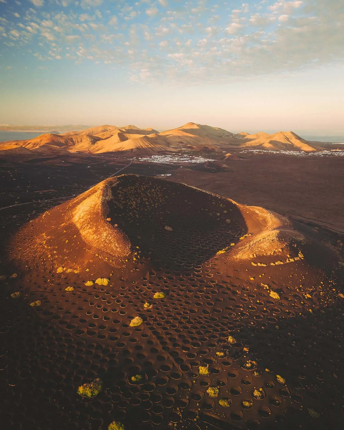 Panorama de volcans endormis et de champs de lave dans le Parc Naturel des Volcans à Lanzarote, baigné par une lumière de fin de journée.