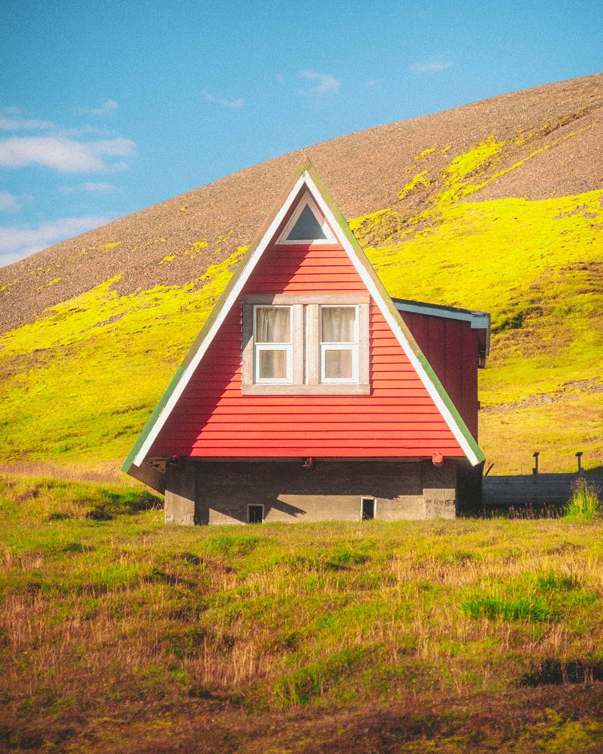 Le refuge A-frame rouge iconique du camp de base de Kerlingarfjöll, contrastant avec les montagnes rhyolitiques fumantes des Hautes Terres.