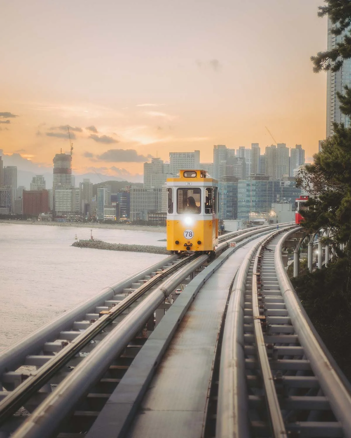Wagon jaune du Sky Capsule longeant la côte de Haeundae à Busan au crépuscule. Attraction incontournable de Corée du Sud capturée avec un bokeh urbain.