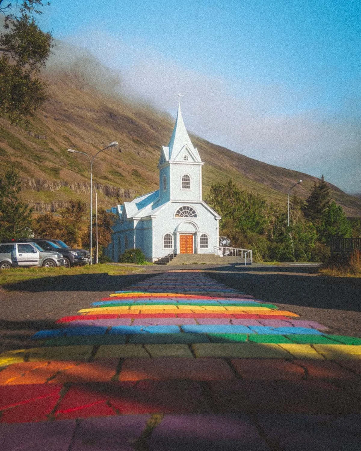La célèbre église bleue (Seyðisfjarðarkirkja) et son chemin arc-en-ciel à Seyðisfjörður, dans les fjords de l'Est de l'Islande. Photo de voyage colorée par Dimitri Weber.