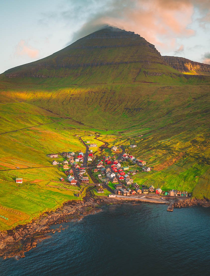 Vue aérienne époustouflante d'un village côtier niché au pied d'une montagne verte aux Îles Féroé. Photographie de voyage grand espace.