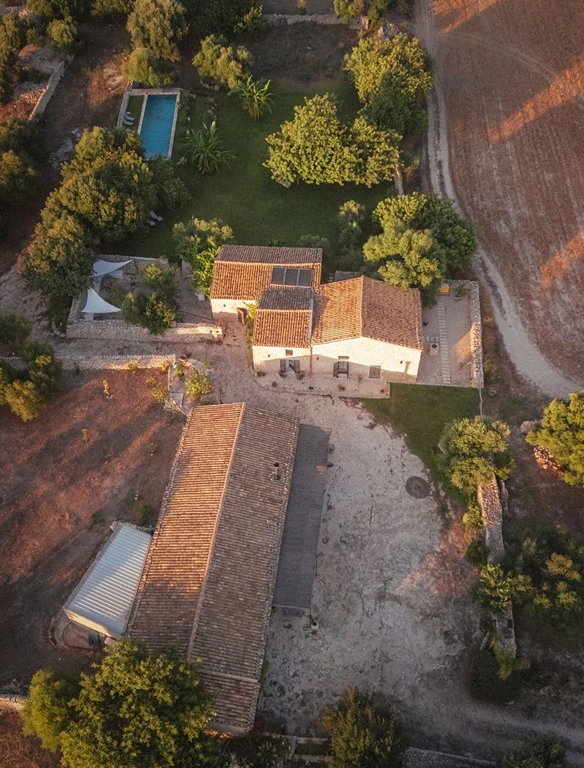 Vue aérienne verticale (Top-down) d'un Mas en pierre avec piscine et jardin paysager au coucher du soleil. Photographie immobilière de prestige et touris