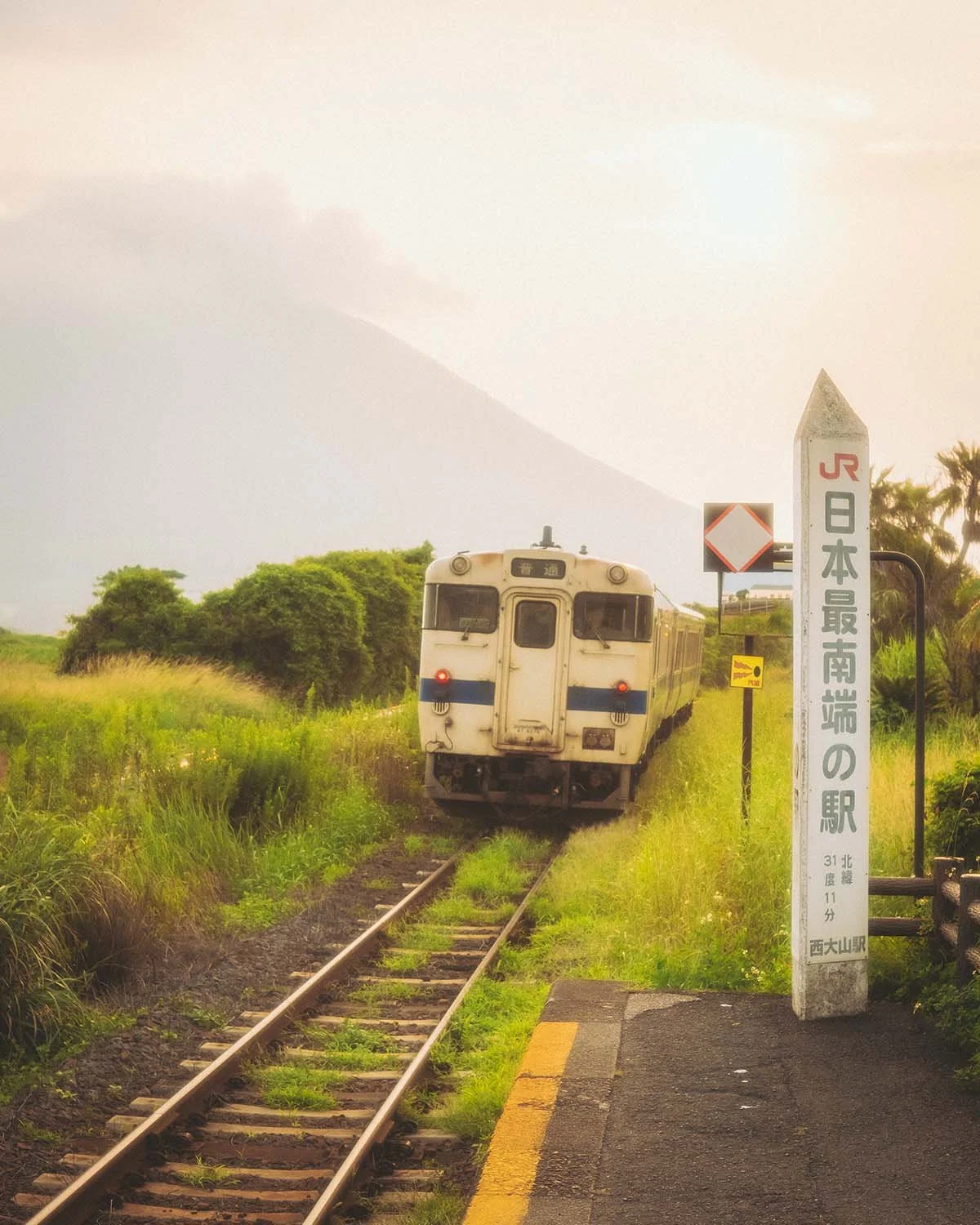 Train local arrivant à la gare de Nishi-Oyama, la gare JR la plus au sud du Japon, avec le volcan Mont Kaimon en arrière-plan. Photo de voyage ferroviaire par Dimitri Weber.