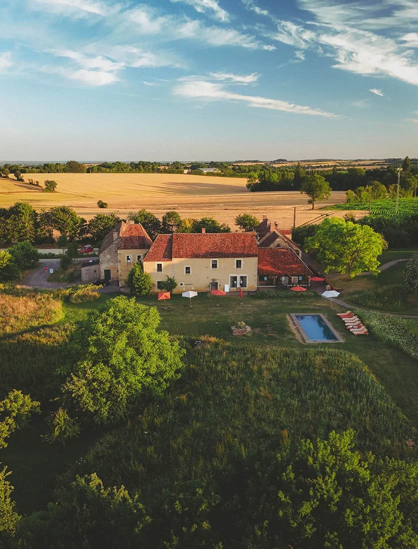 Vue aérienne globale d'un domaine touristique avec piscine au milieu des champs. Valorisation de destination rurale et hôtellerie de charme.