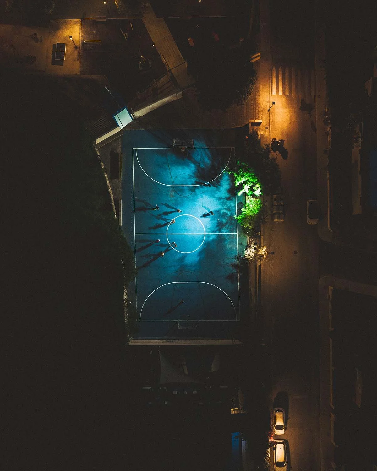 Playground nocturne. Sous le halo des lampadaires, le terrain vide attend ses joueurs dans la chaleur de la nuit.