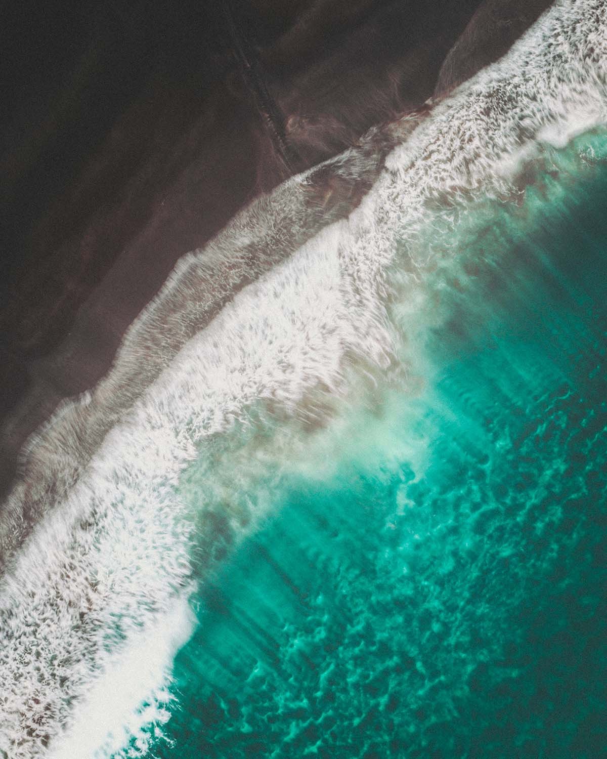 Ambiance "moody" sur une plage de sable noir volcanique aux Îles Féroé. Contraste entre l'écume blanche des vagues et le rivage sombre vu par drone.