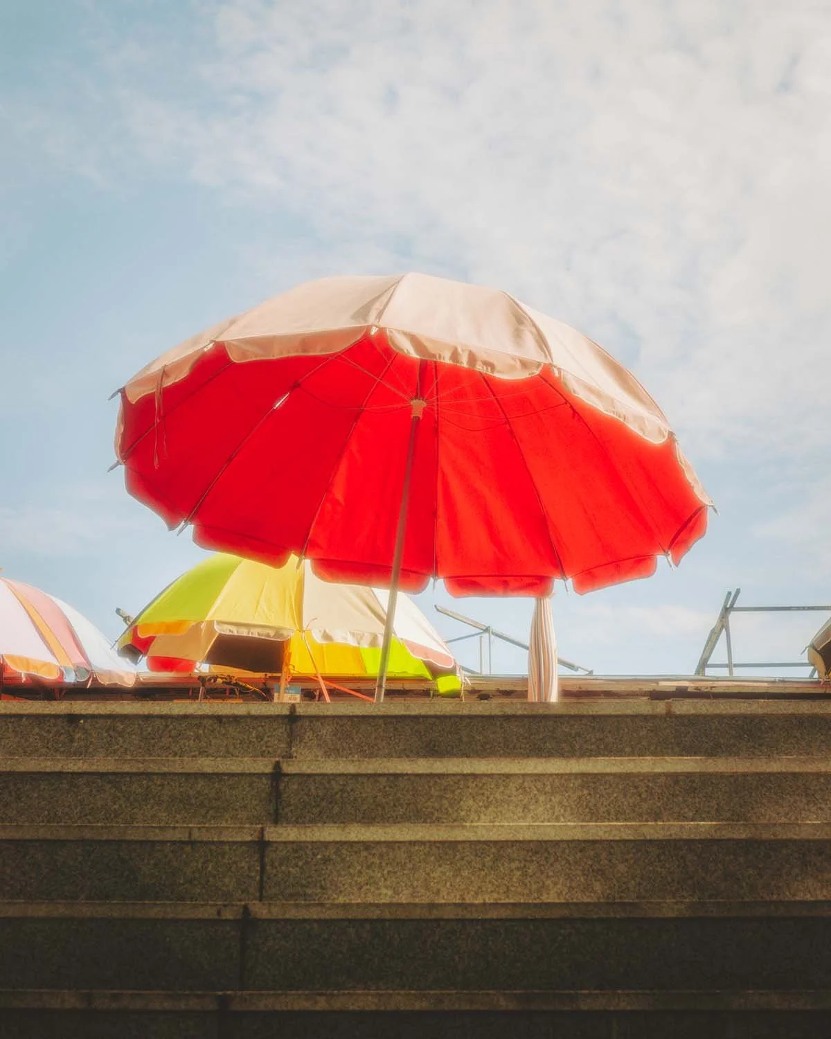 Composition photographique minimaliste d'un parasol rouge ouvert sur des marches en pierre, évoquant l'été et la chaleur en bord de mer au Japon.