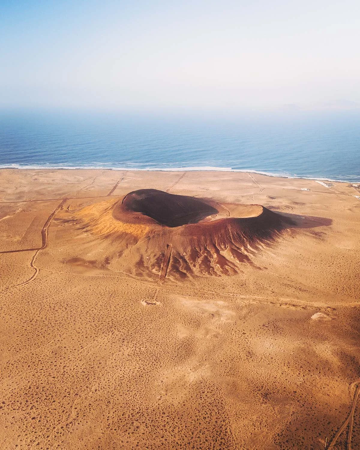 Vue aérienne impressionnante du cratère rouge du volcan Calderón Hondo à Fuerteventura, entouré par l'océan Atlantique et le désert.