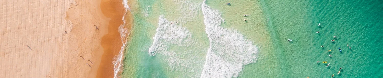 Inspiration lune de miel : vue aérienne graphique et apaisante d'une plage aux eaux turquoises avec surfeurs. Portfolio Voyage et Lifestyle.