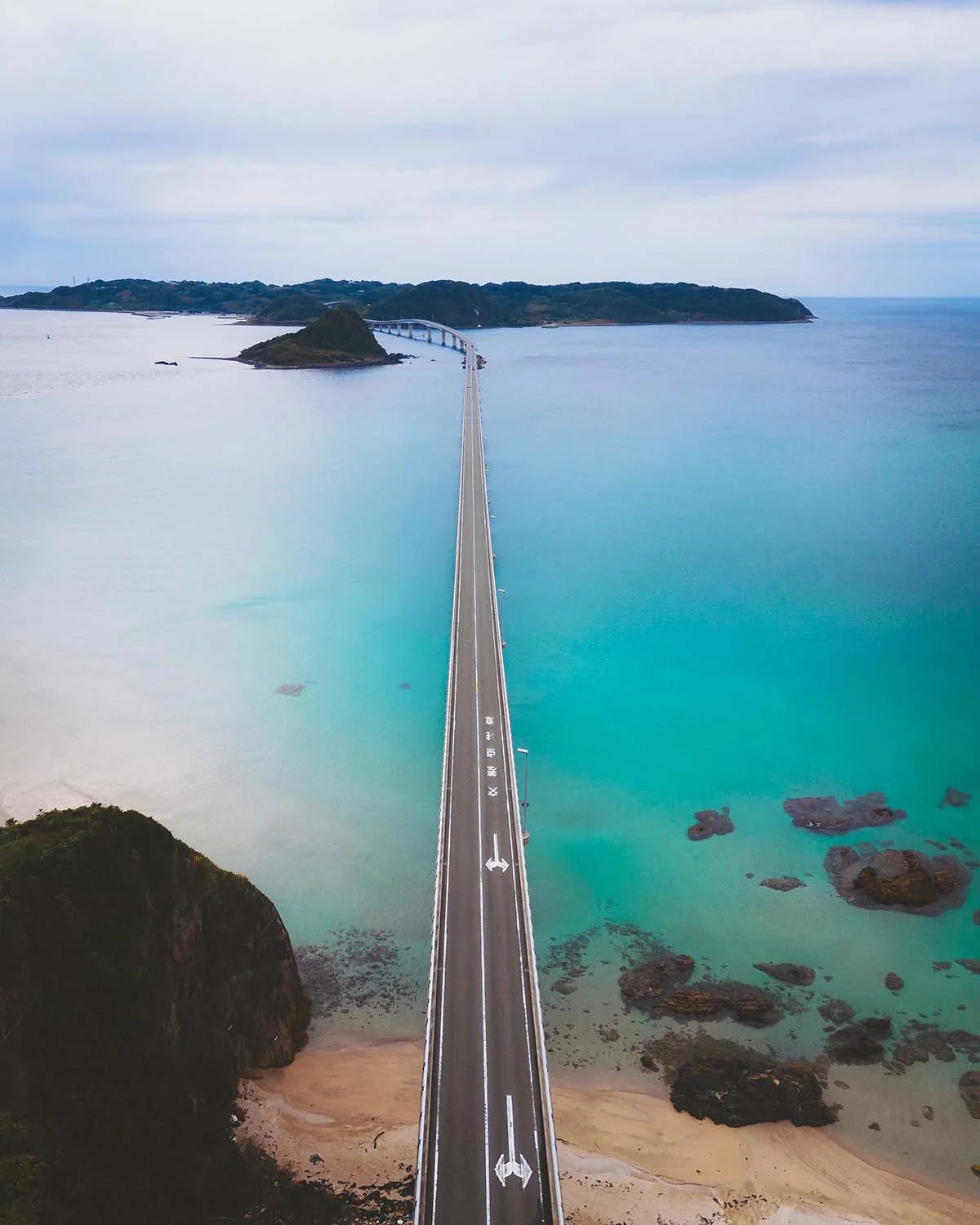 Photographie aérienne rectiligne du pont Tsunoshima traversant une mer bleu turquoise dans la préfecture de Yamaguchi. Un des plus beaux spots de road trip au Japon.