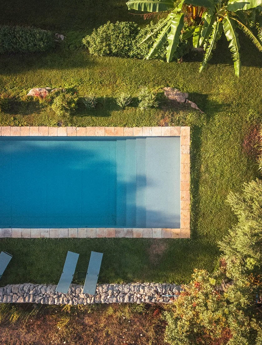 Photo graphique d'une piscine vue du ciel, mettant en valeur la clarté de l'eau, la pierre naturelle et la végétation tropicale.
