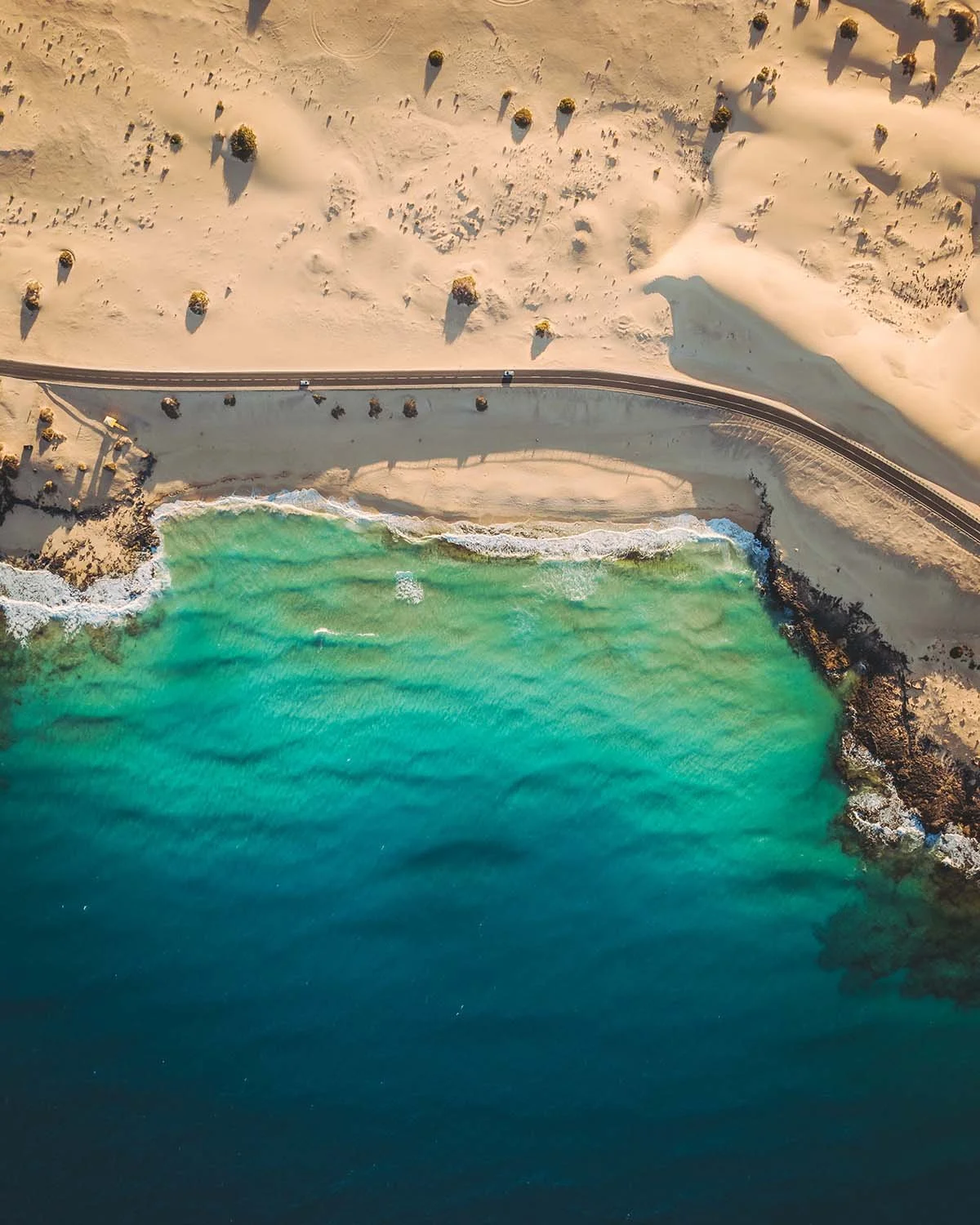 La célèbre route FV-1 longeant la côte à Fuerteventura, séparant les dunes de sable blanc de l'eau turquoise. Image parfaite pour illustrer un road trip.