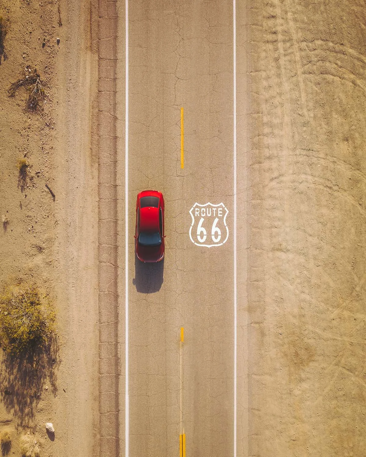 Vue verticale top down drone logo Route 66 peint sur asphalte route déserte Californie Arizona. Roadtrip voiture rouge solitude désert Mojave Mother Road voyage USA car culture.