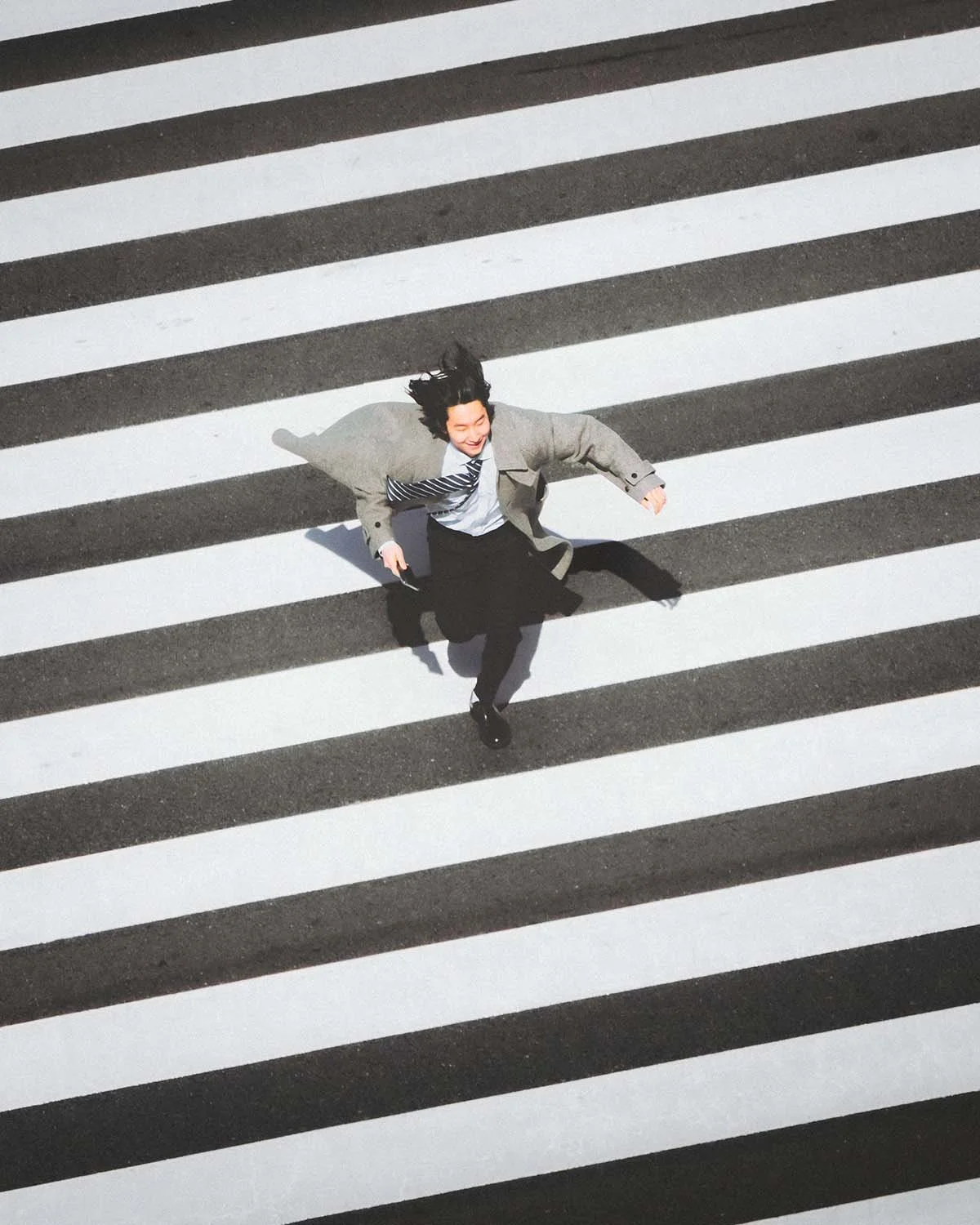 Photographie de rue dynamique capturant un "salaryman" japonais courant joyeusement sur un passage piéton zébré à Tokyo. Mouvement et vie urbaine.