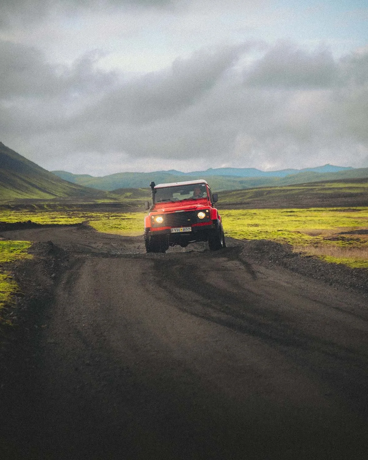 Un vieux Land Rover Defender rouge explorant la piste F225 (Landmannaleið) au milieu des paysages volcaniques. L'essence du road trip aventure en Islande.