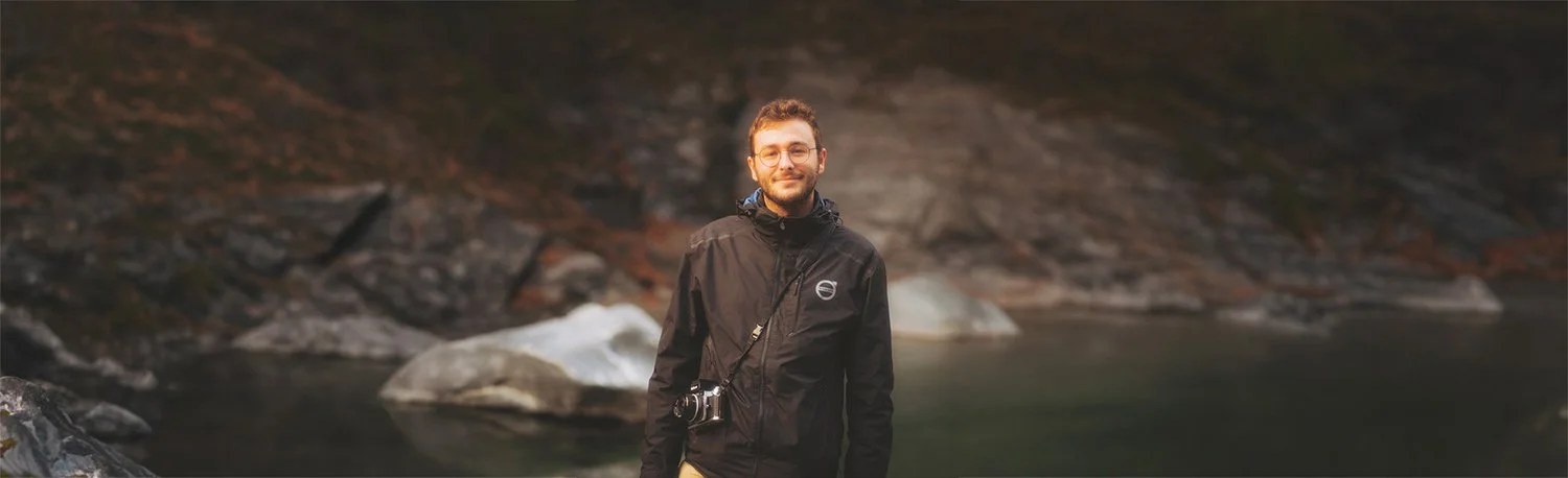 Portrait souriant de Dimitri Weber, photographe et vidéaste professionnel basé en Île-de-France, portant un appareil photo en bandoulière. Image de présentation du fondateur.