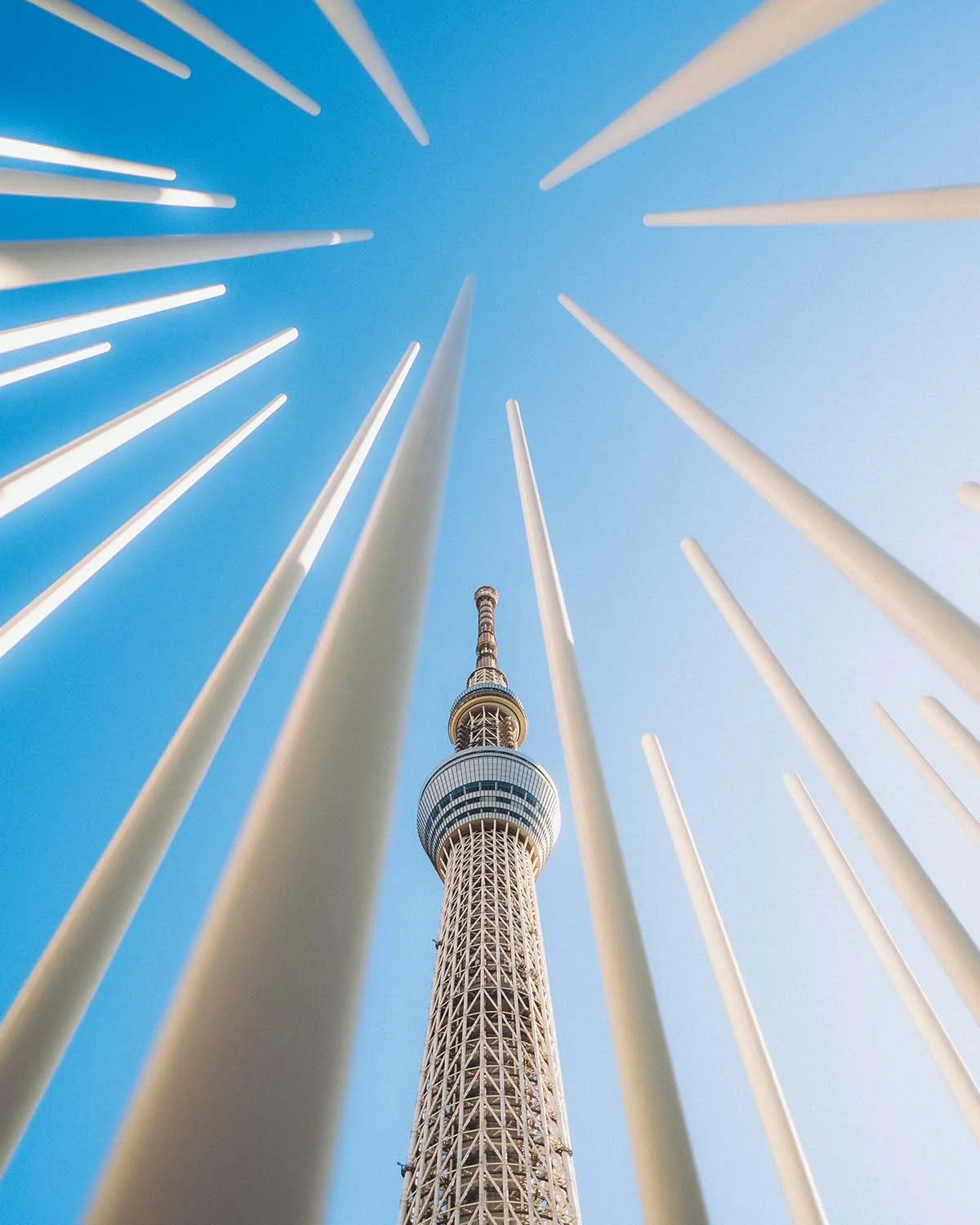 Architecture moderne Tokyo Skytree vue en contre-plongée à travers poteaux blancs graphiques ciel bleu. Tour de radiodiffusion quartier Sumida Oshiage design urbain minimaliste voyage Japon.