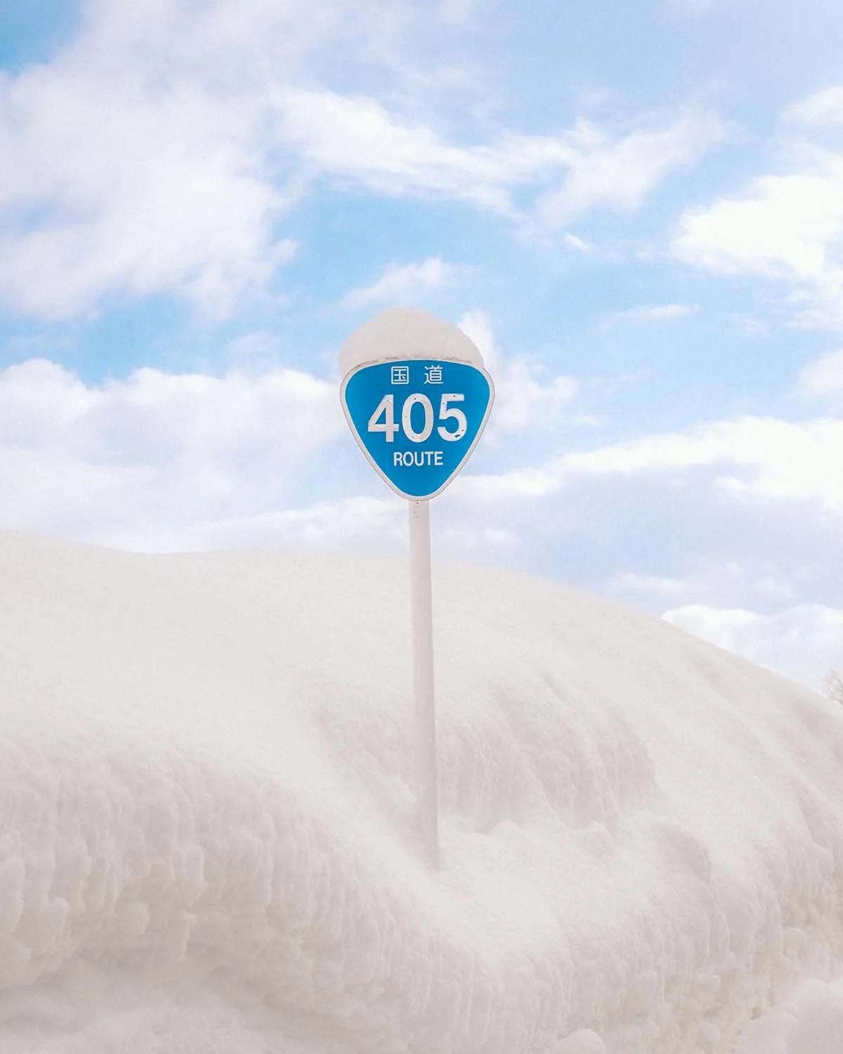 Panneau bleu de la Route Nationale 405 (R405) émergeant à peine d'une épaisse couche de poudreuse. Illustration de l'hiver rigoureux dans les "Snow Country" du Japon (Niigata/Gunma).