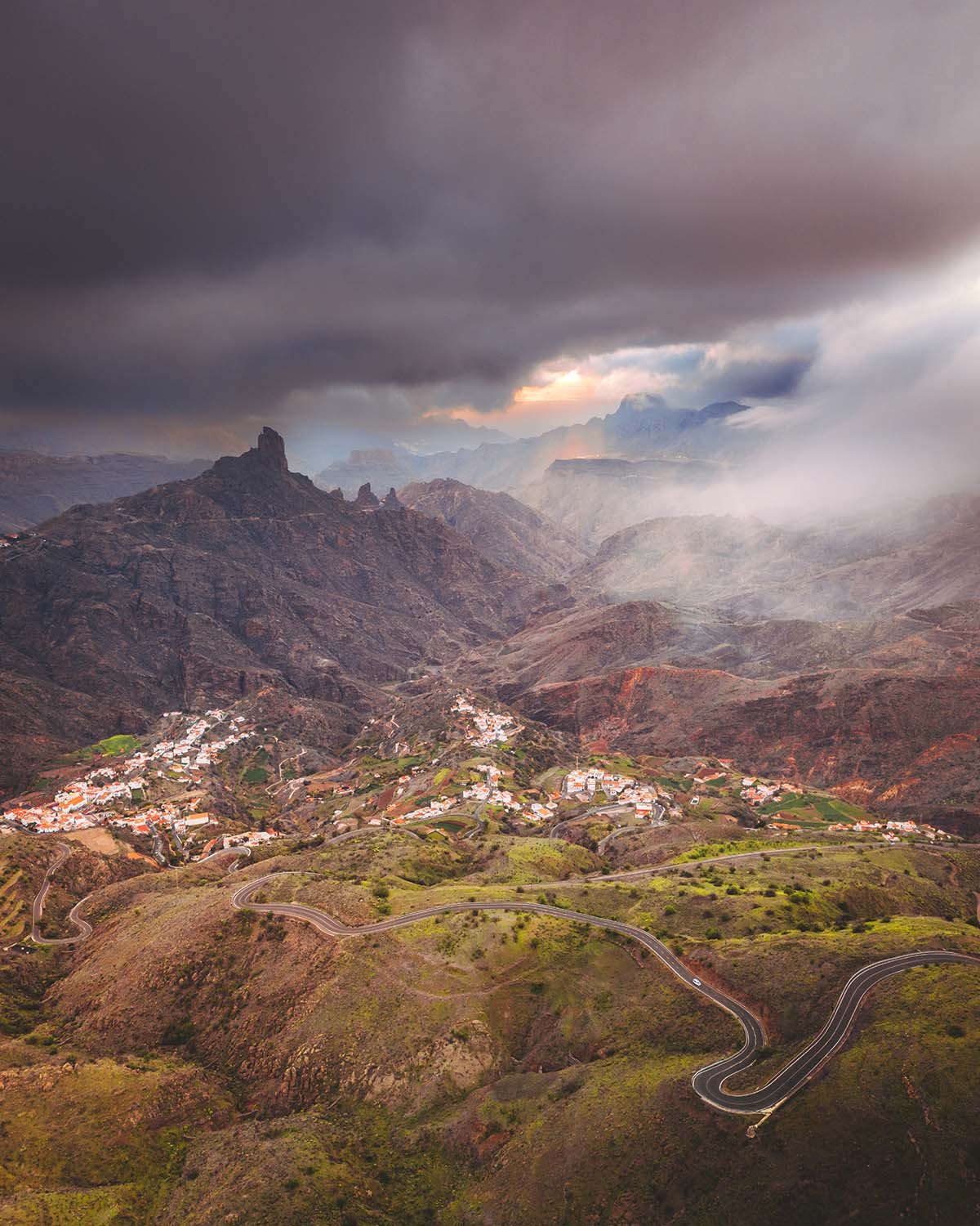 Route en lacet traversant une vallée montagneuse spectaculaire sous un ciel orageux. Paysage de randonnée épique aux Canaries (type Gran Canaria ou Tenerife).