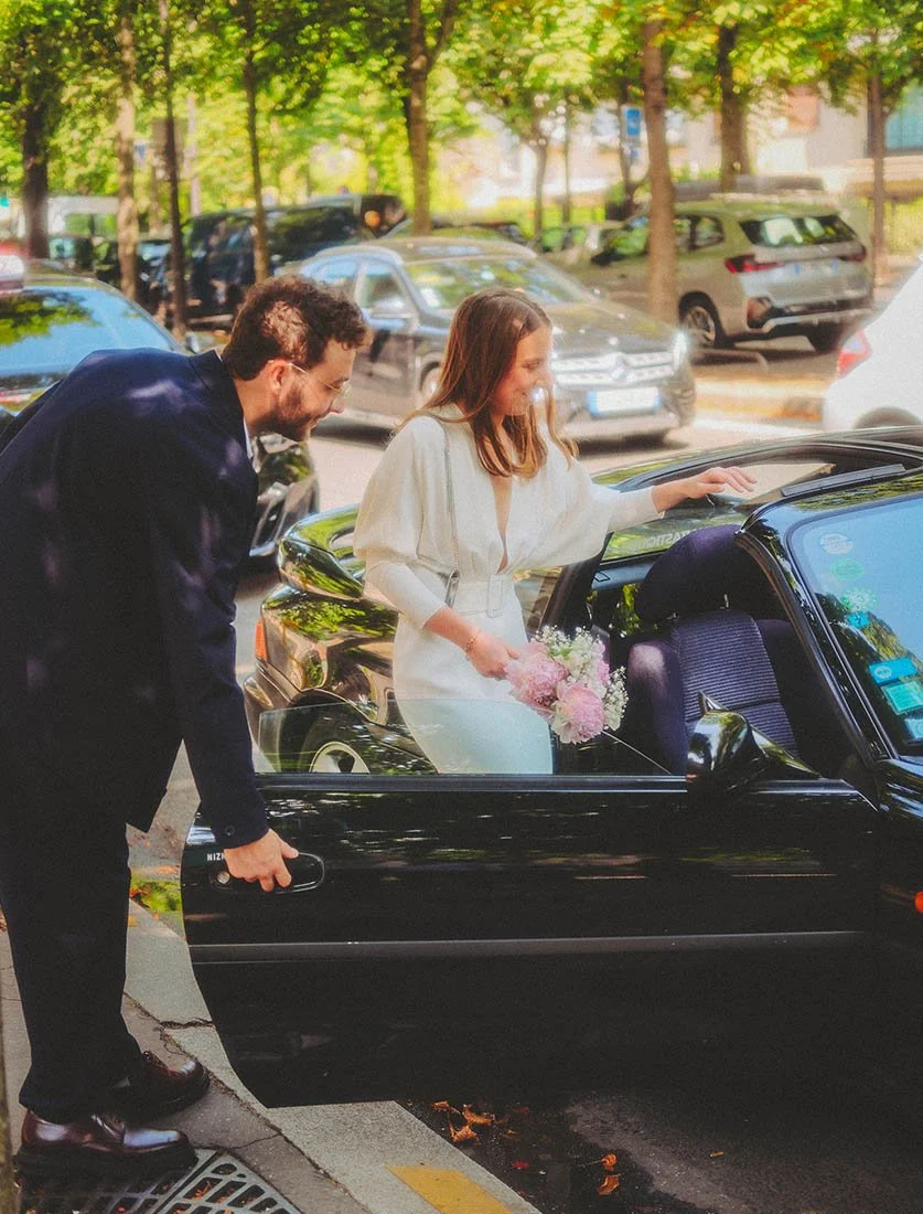 Mariage moderne et passion automobile : la mariée montant dans une voiture de sport japonaise (type RX7/Supra) conduite par le marié.