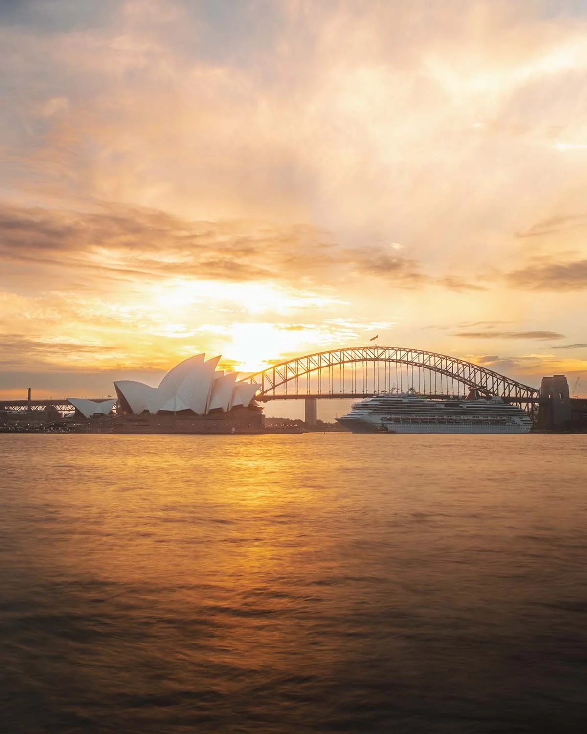 Vue iconique du port de Sydney au coucher du soleil, réunissant l'Opéra de Sydney et le Harbour Bridge sous une lumière dorée. Photographie de paysage urbain australien.