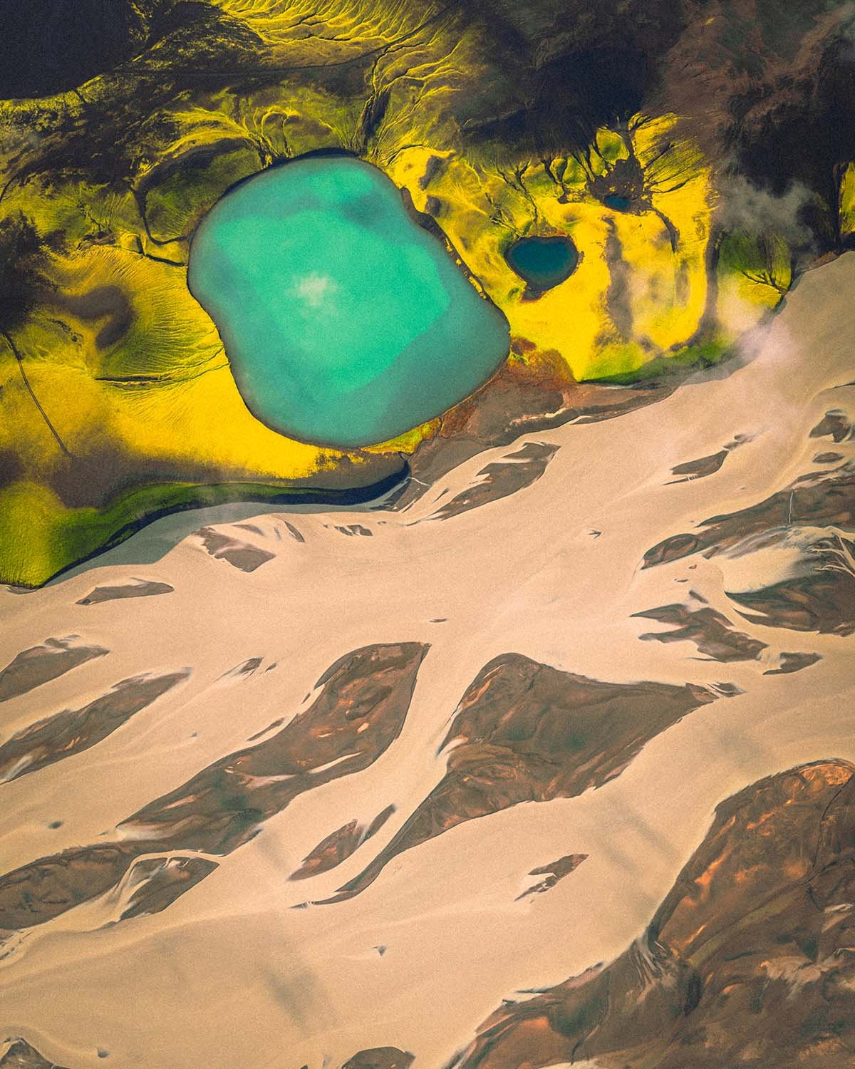 Vue aérienne d'un lac alpin alimenté par des rivières glaciaires tressées (braided rivers) formant des motifs complexes le long de la F208.