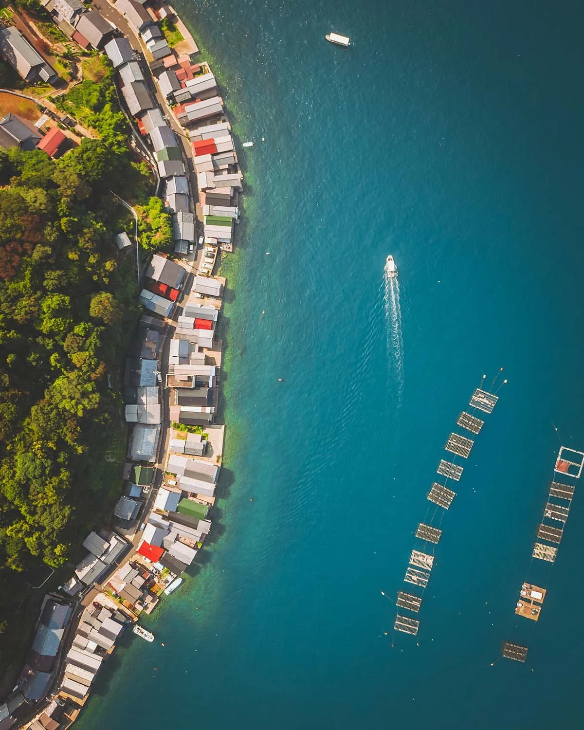 Vue aérienne verticale (top-down) par drone des maisons-bateaux traditionnelles (Funaya) d'Ine, dans la préfecture de Kyoto, montrant l'eau émeraude et les filets de pêche.