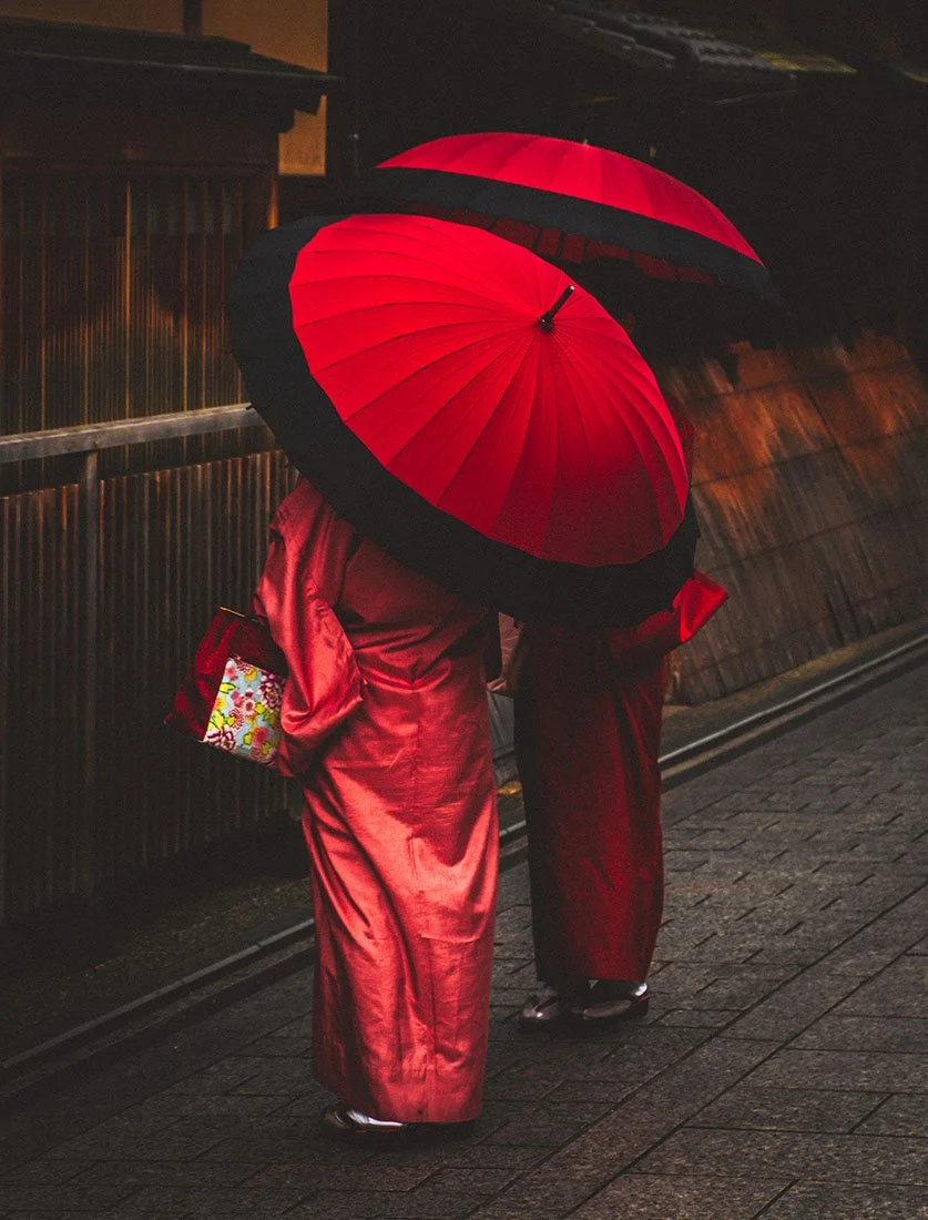 L'élégance traditionnelle japonaise : deux femmes en kimono sous des ombrelles rouges dans une rue historique de Kyoto. Photographie de voyage culturelle.