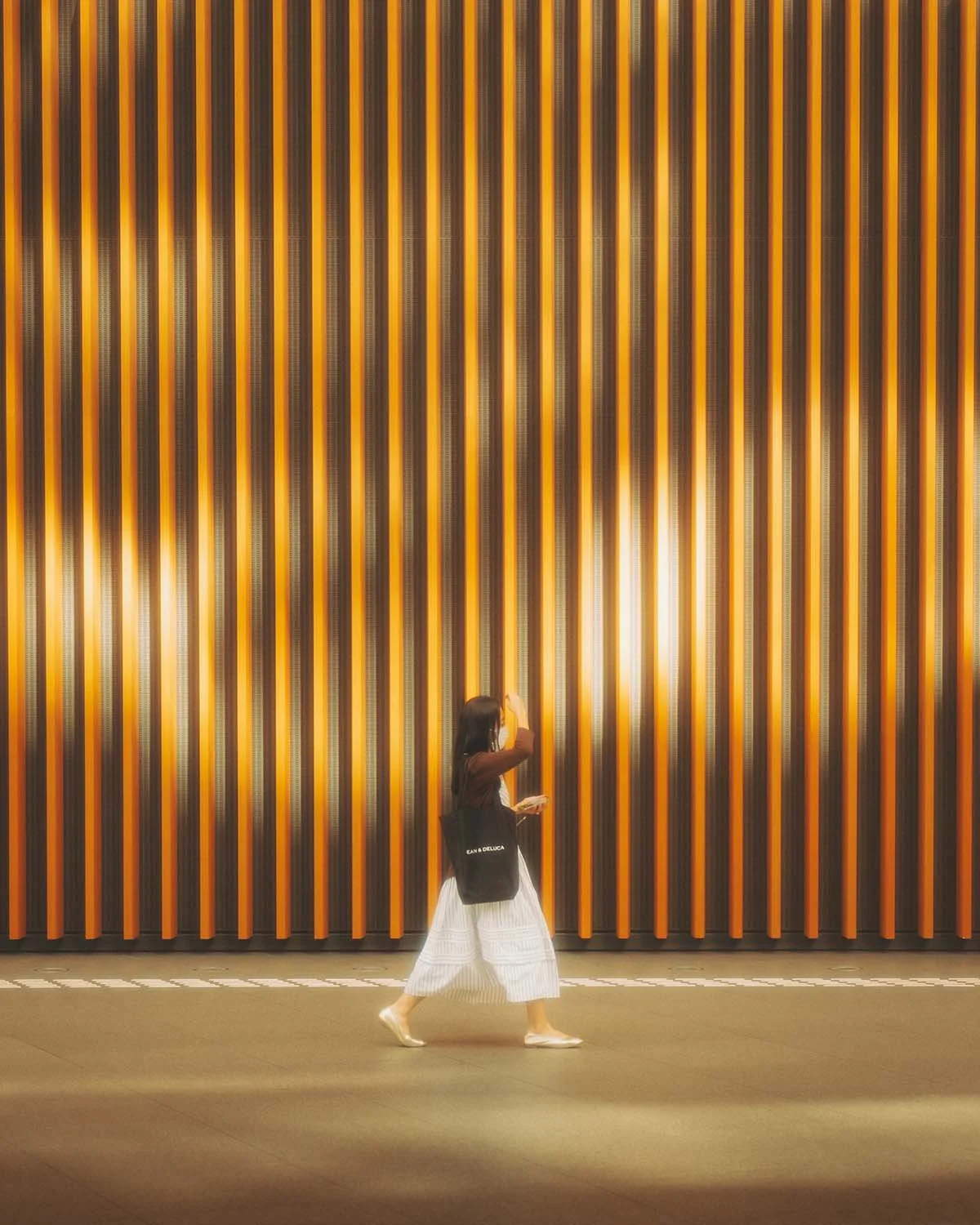 Photo de rue artistique jouant sur le contraste entre une silhouette féminine en mouvement et un arrière-plan architectural composé de lignes verticales orangées et noires.