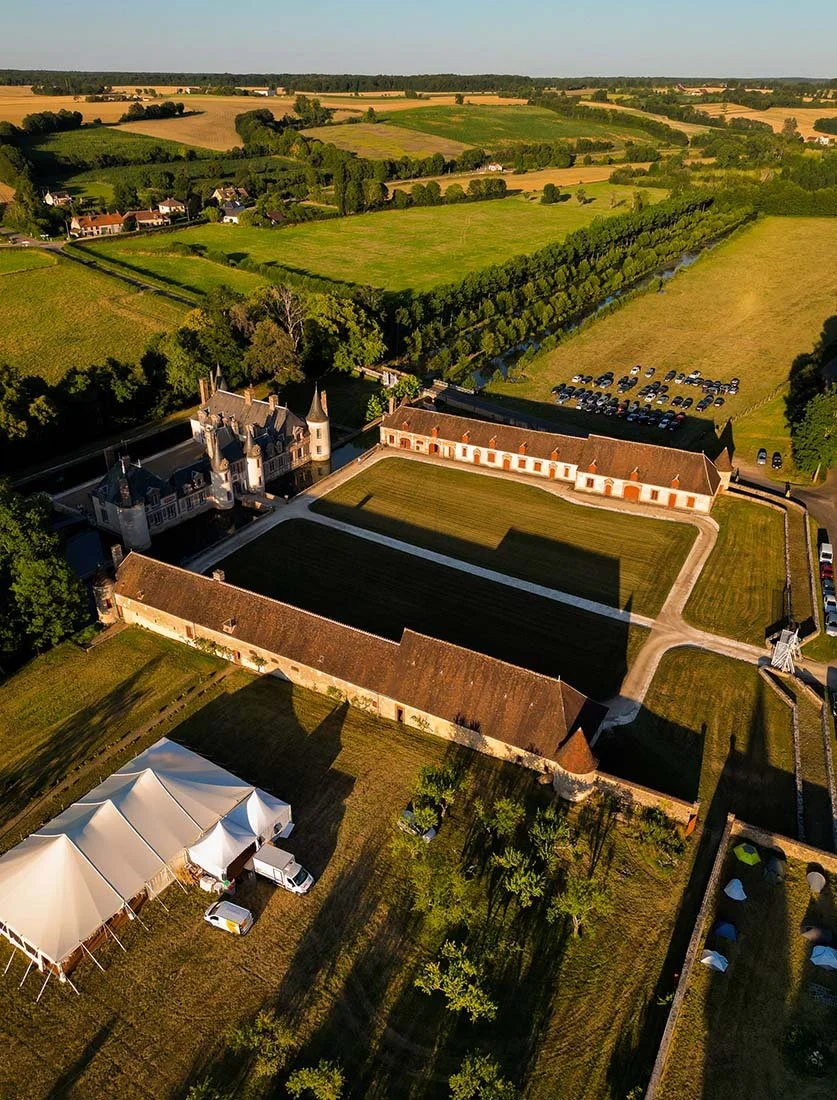 Vue aérienne majestueuse d'un château historique entouré de douves, accueillant une réception de mariage sous chapiteau. Photographie de patrimoine et d'événementiel.