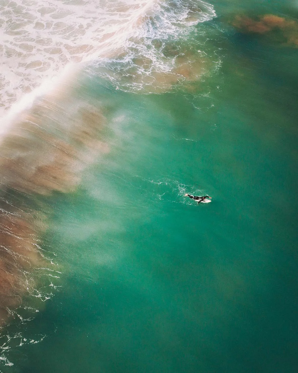 Seul face à l'immensité. Un surfeur rame vers le large, point minuscule dans une étendue d'émeraude.