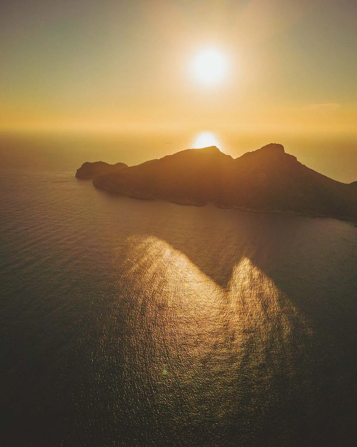 Contre-jour insulaire. La silhouette massive d'une île se découpe sur l'or liquide du soleil couchant.