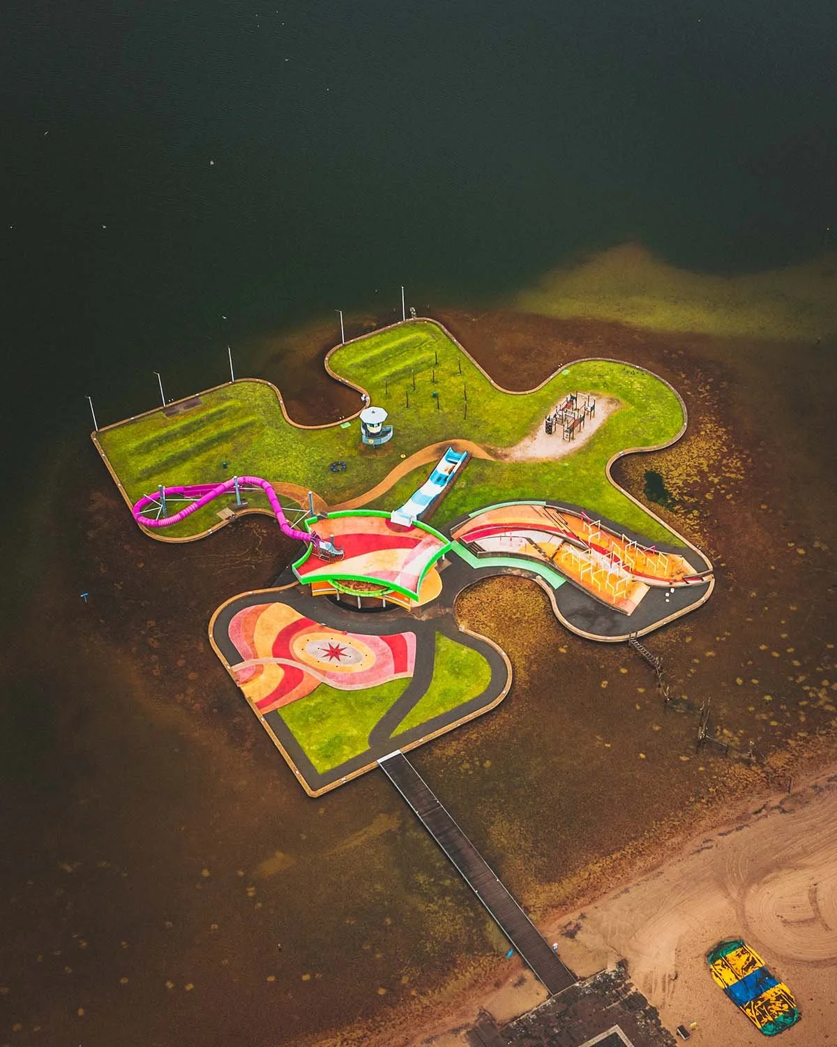 La pièce manquante. Un parc aquatique en forme de puzzle coloré flotte graphiquement sur le lac.