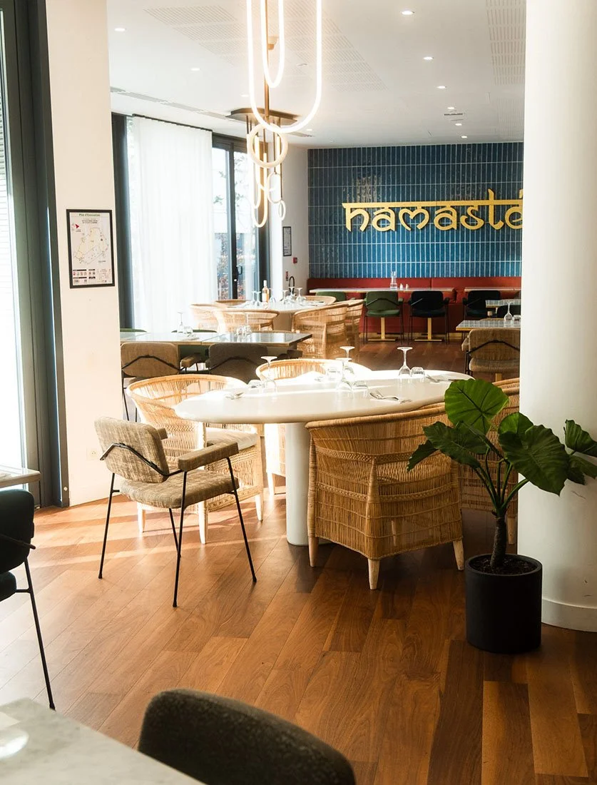 Vue d'ensemble d'une salle de restaurant lumineuse au design contemporain (rotin, plantes). Mise en valeur des espaces d'accueil pour l'hôtellerie-restauration.