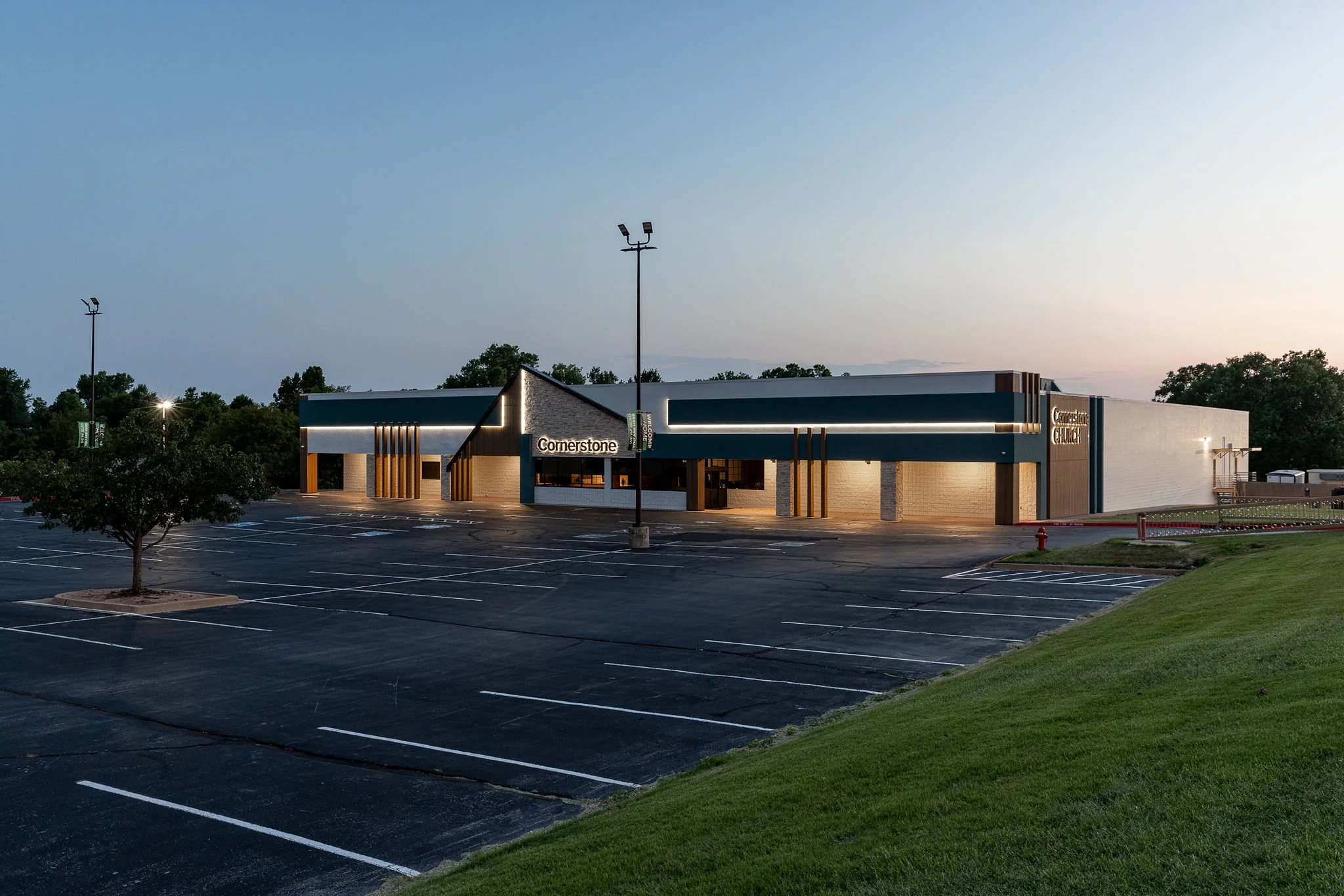 Empty parking lot outside a modern church building at dusk with trees in the background.