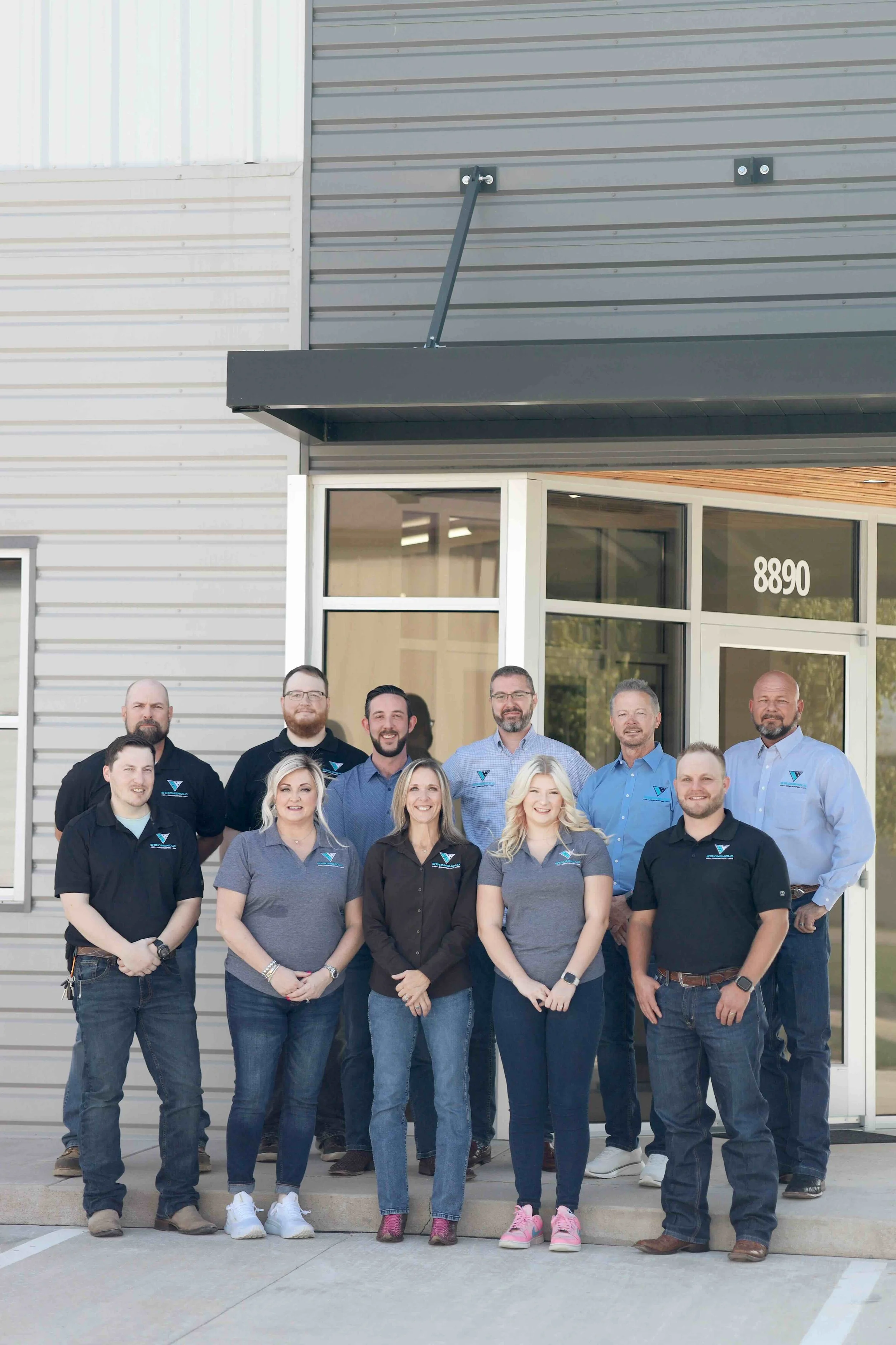 Group of ten people standing outside a building with the address 8890, posing for a photo.