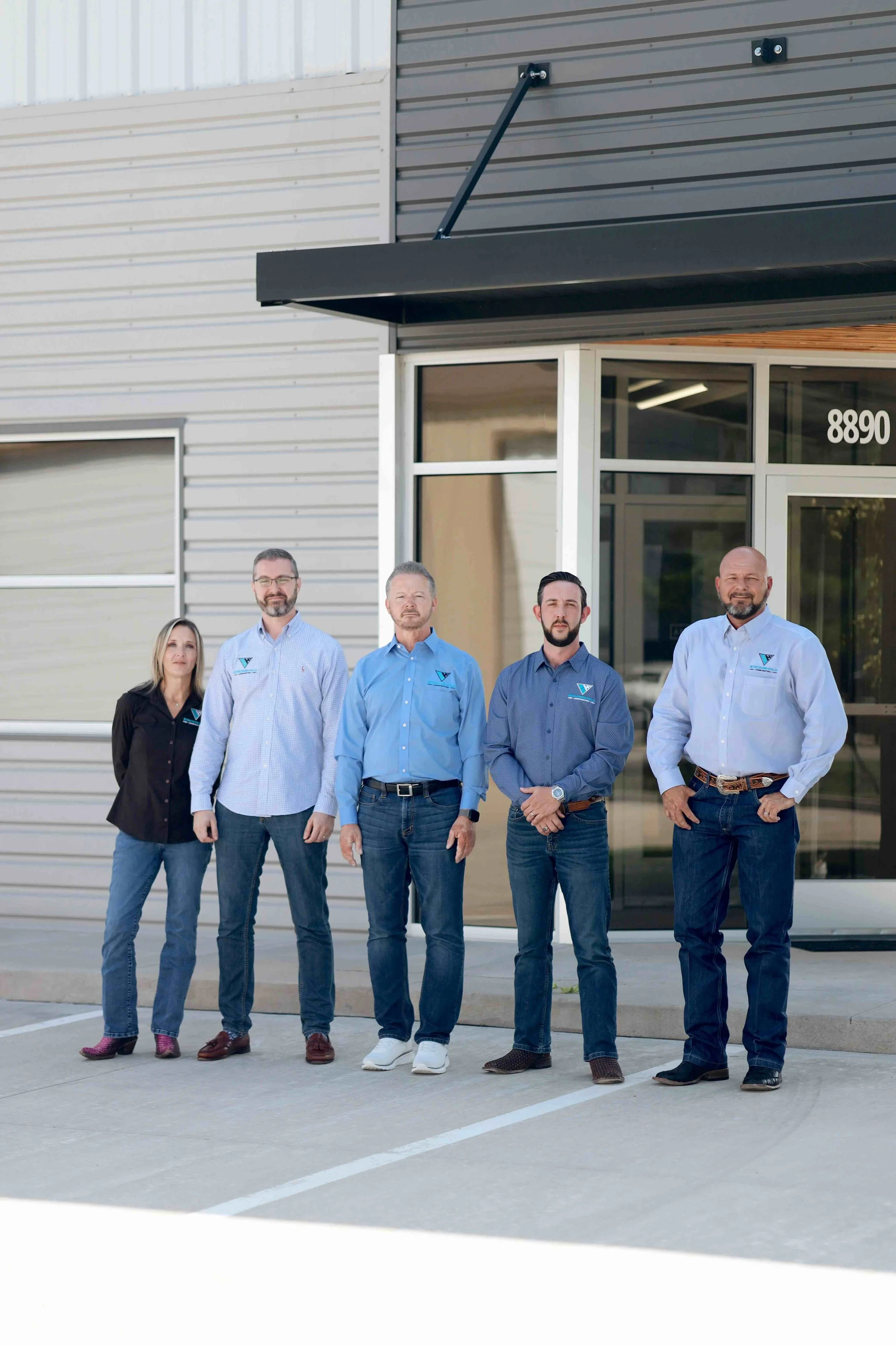 Group of five people standing outside a commercial building with a glass entrance, posing for a photo.