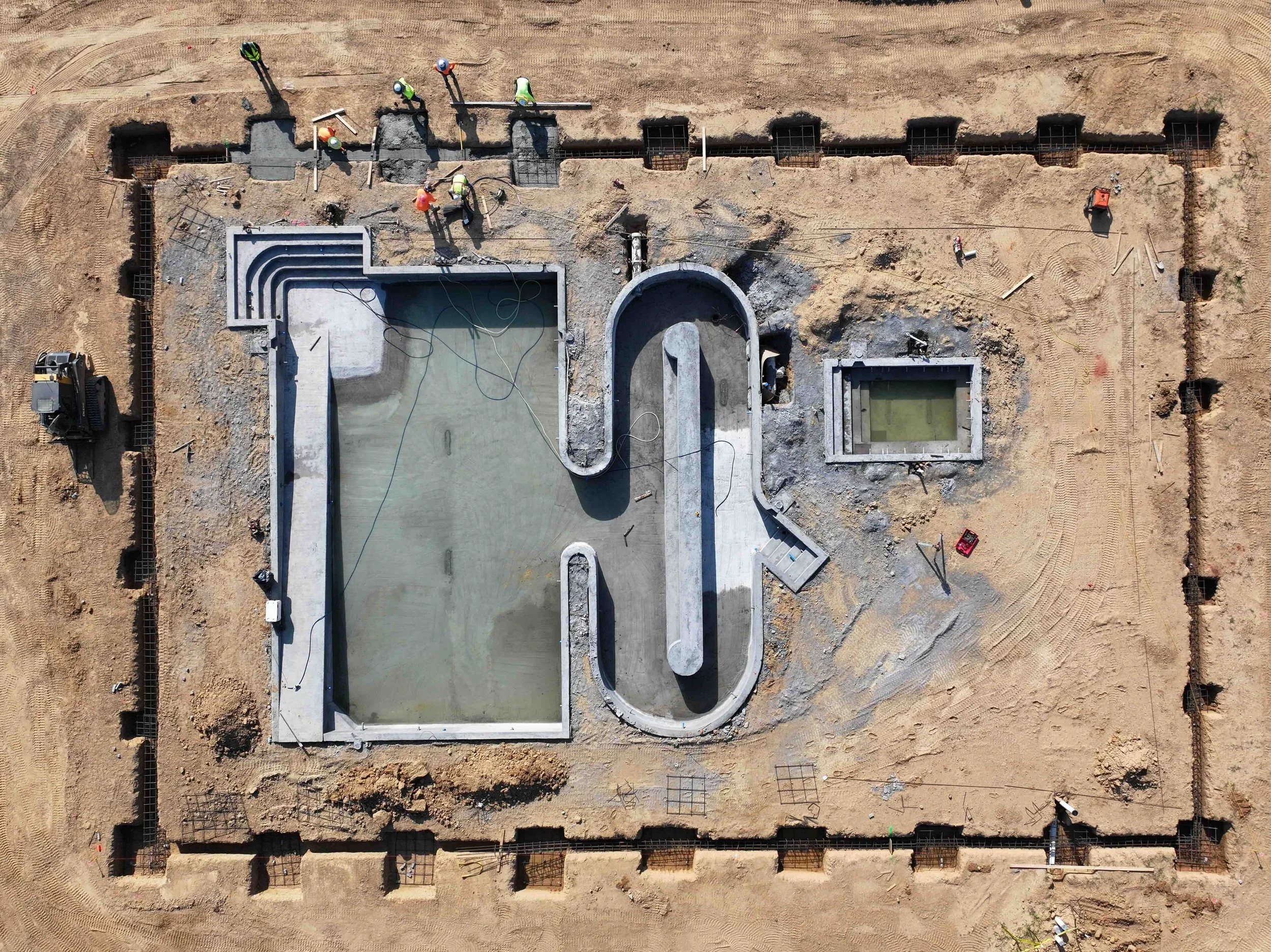 Aerial view of a swimming pool construction site with workers, construction equipment, and exposed rebar.