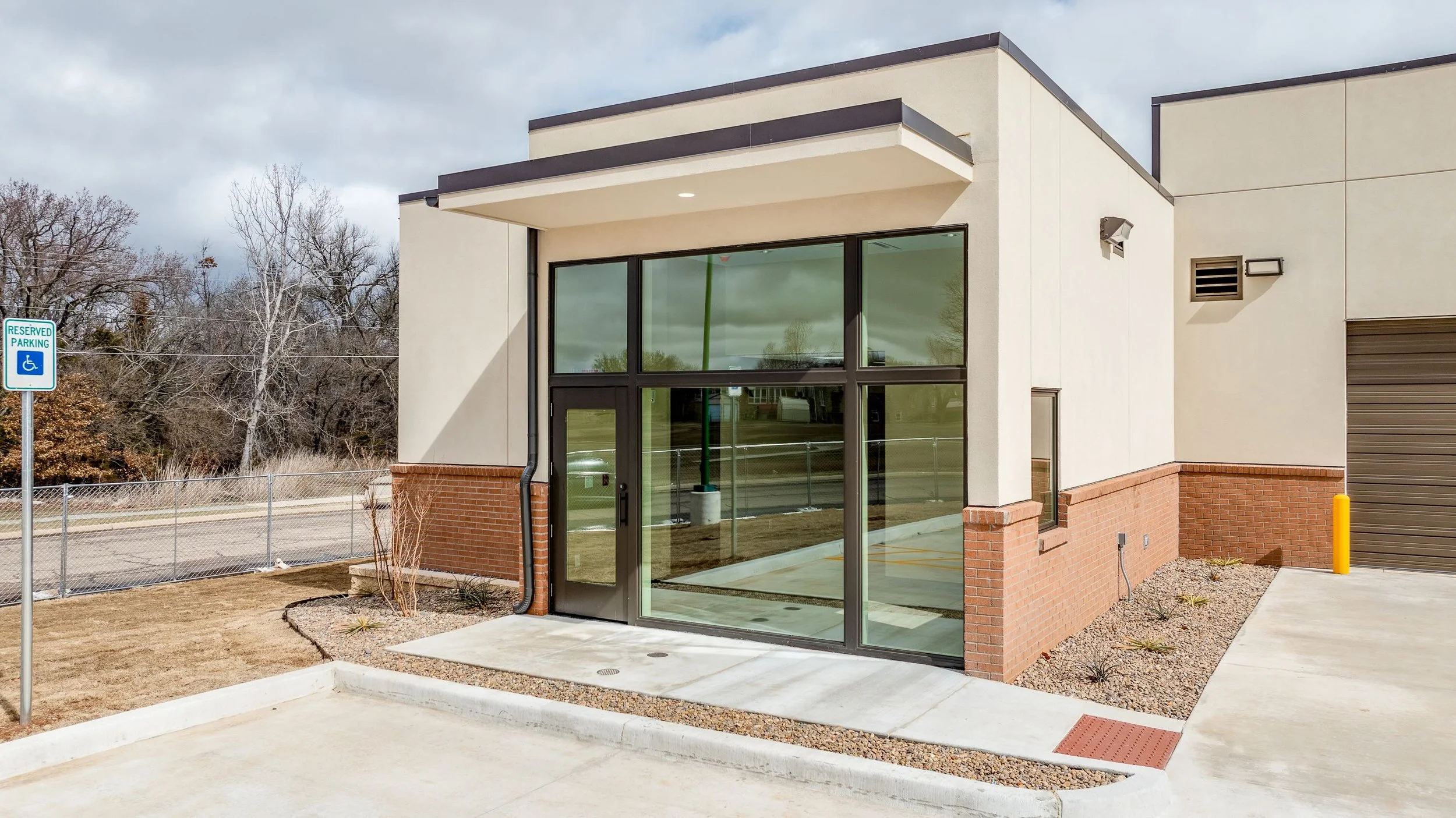 Commercial building with large glass windows and a glass door, brick and stucco exterior, parking lot, and designated accessible parking space.