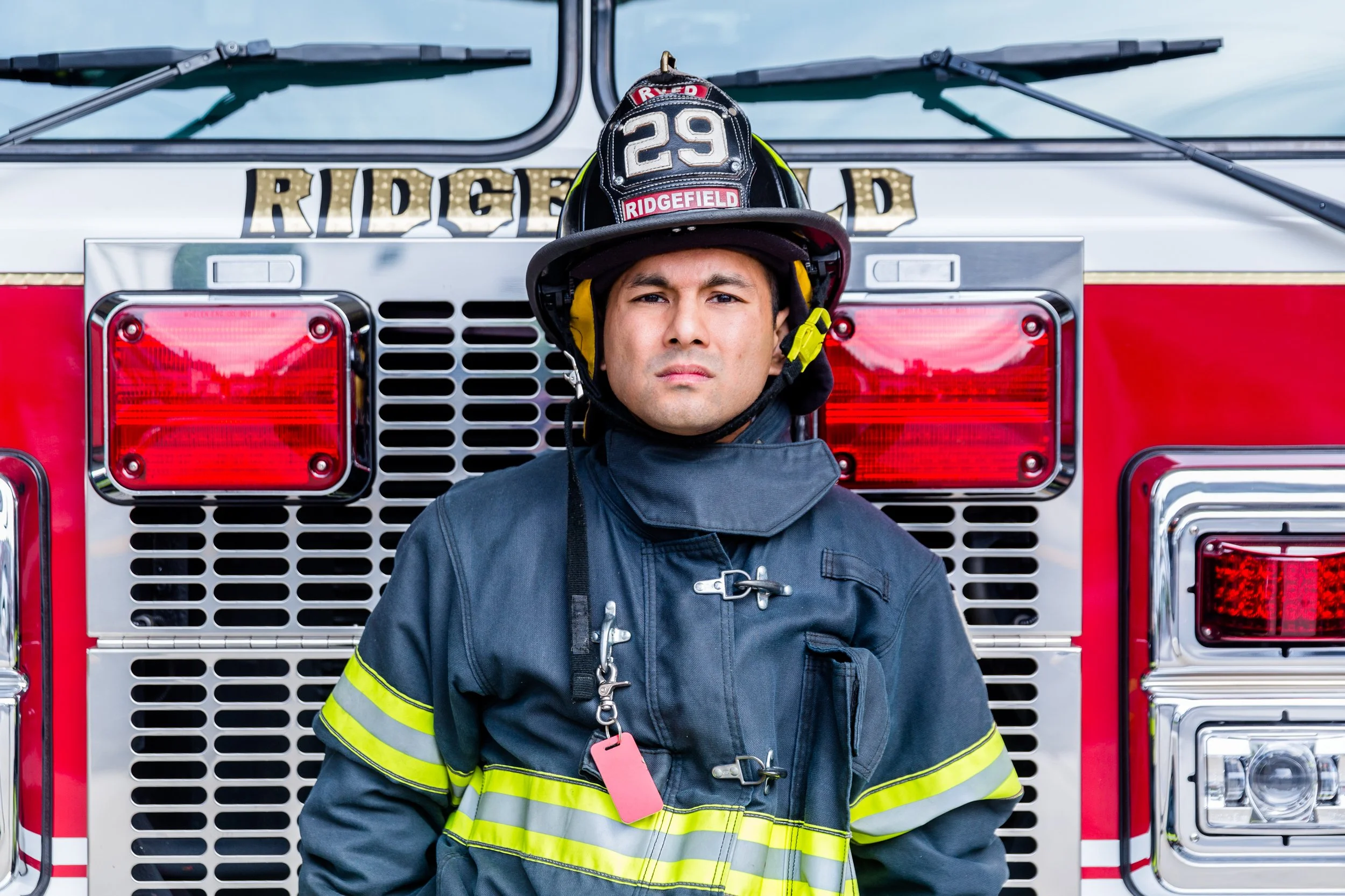 Firefighter standing in front of a fire truck, wearing a helmet and uniform.