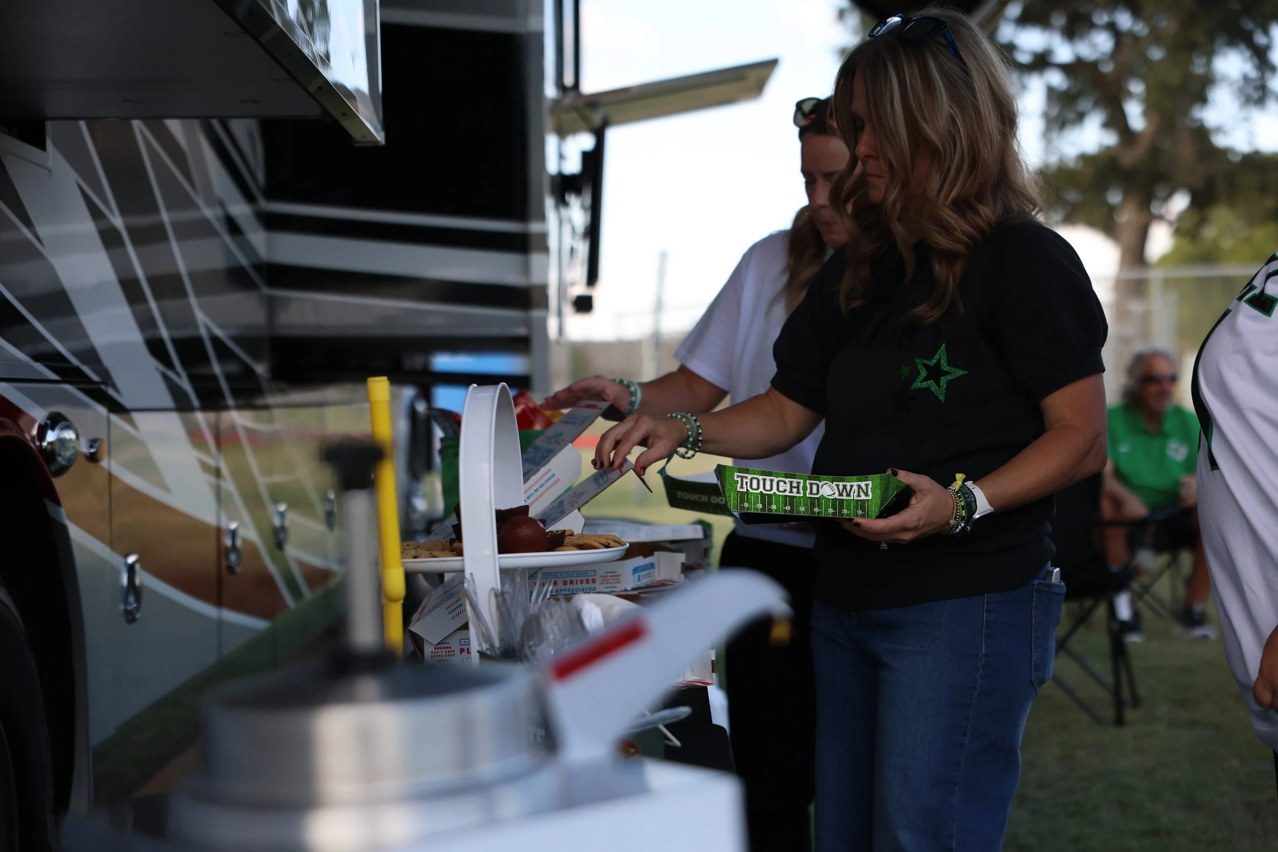 People at a food truck selecting food, with one person holding a box that says 'Touch Down' and eating utensils visible on the counter.