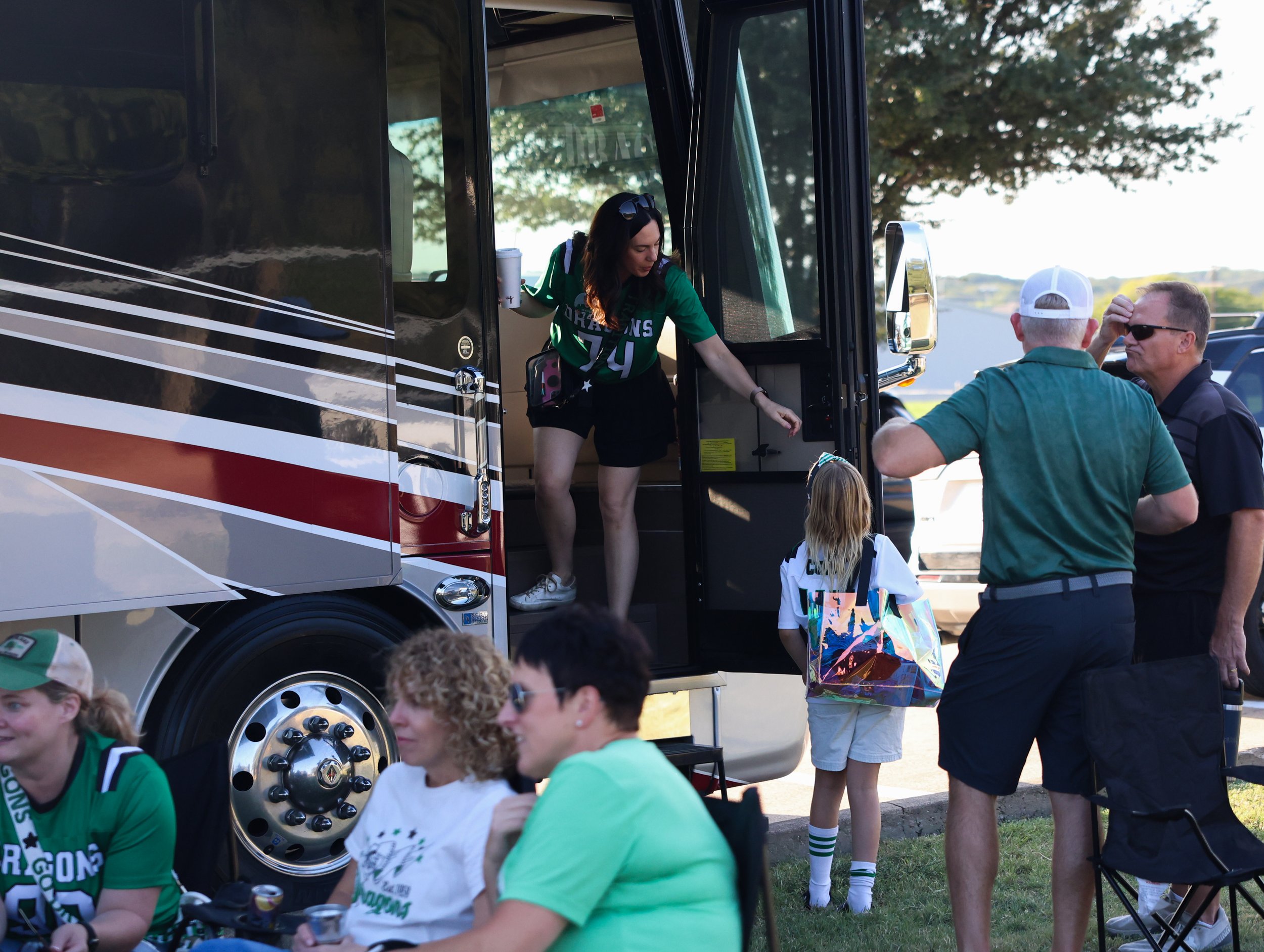 A woman getting off a bus with a woman and children, surrounded by people in a parking lot during daytime.