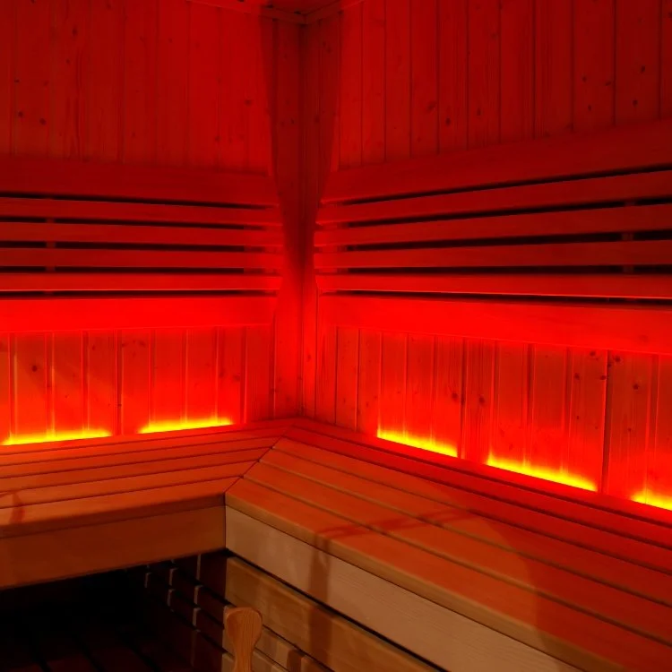 Interior corner of a wooden sauna with red lighting along the lower edges and horizontal wooden slats on the walls.