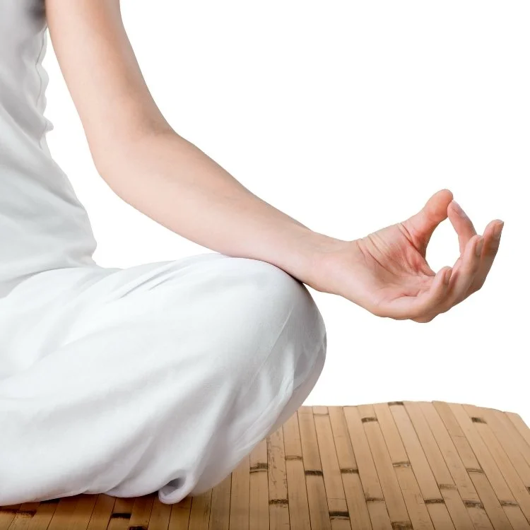 Person practicing meditation or yoga in a seated position on a wooden mat, with a focus on their hand in a mudra gesture.